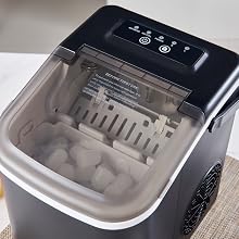 Portable ice maker with clear lid, control panel, and visible ice cube tray. Black and silver design with compact countertop form factor.