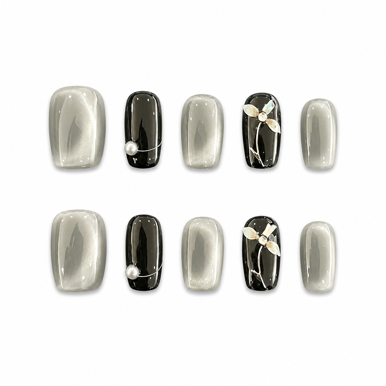 Glossy short square press-on nails featuring silver cat-eye gel, solid black accent nails, a white pearl, and a 3D floral design.