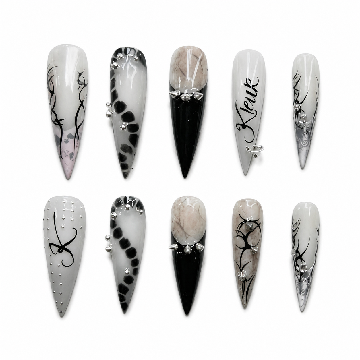 Glossy stiletto press-on nails with black and white gothic tribal art, marble texture, silver cone spikes, and a metal piercing ring.