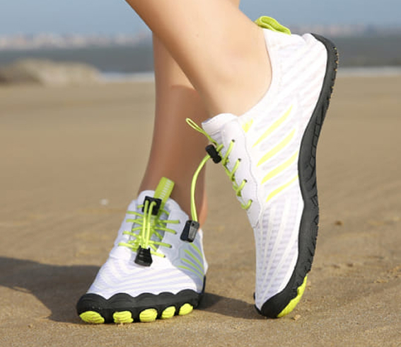 Weiße und neon Grounded Footwear Schuhe, die an einem sandigen Strand getragen werden