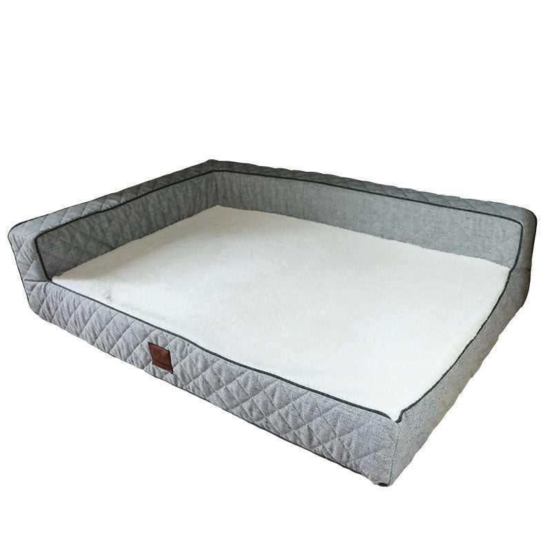 An OrthoLuxe pet mattress shown at an angle against a white background. The bed features quilted grey fabric bolster sides on three edges, a cream-colored memory foam sleeping surface, dark grey piping trim, and a brown leather accent tag on the front. The design combines supportive orthopedic cushioning with raised sides for pets to rest their heads