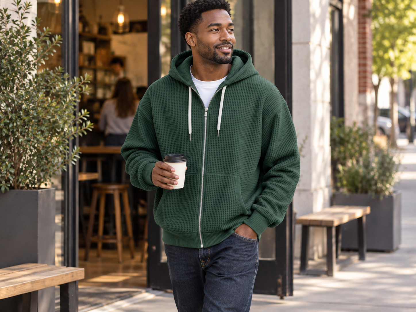 Man wearing the forest green waffle-knit zip-up hoodie outside a coffee shop