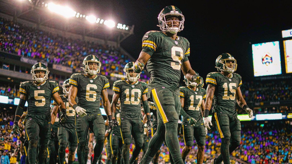 NFL players in green and gold take the field under Thursday night stadium lights