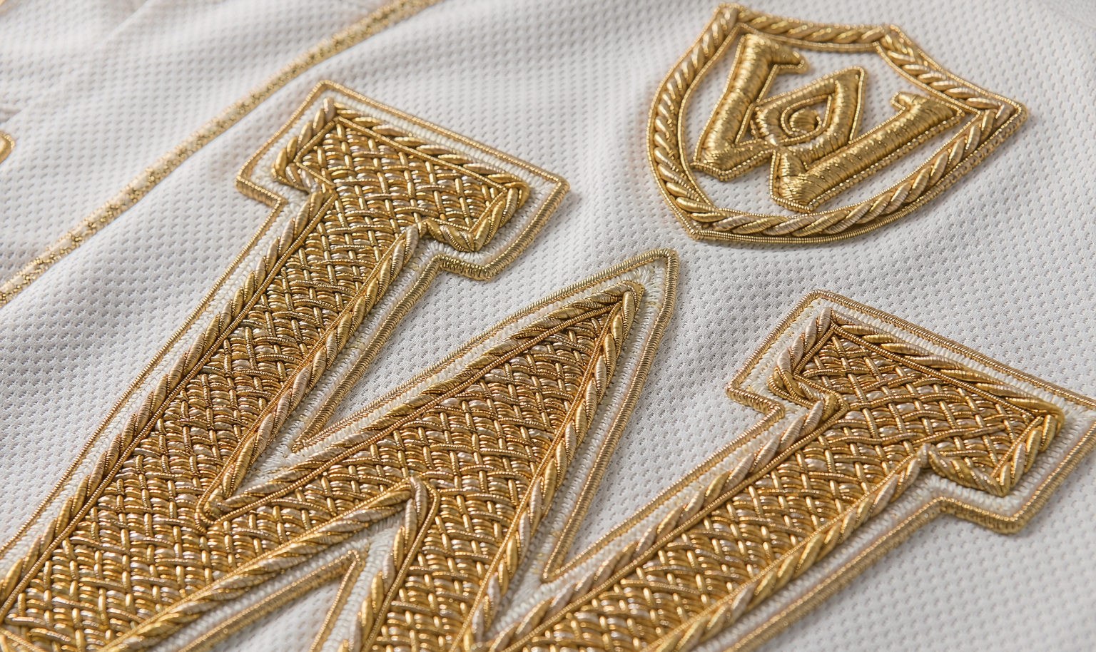 Gold-trimmed numbers and championship patch on a white baseball jersey - macro detail