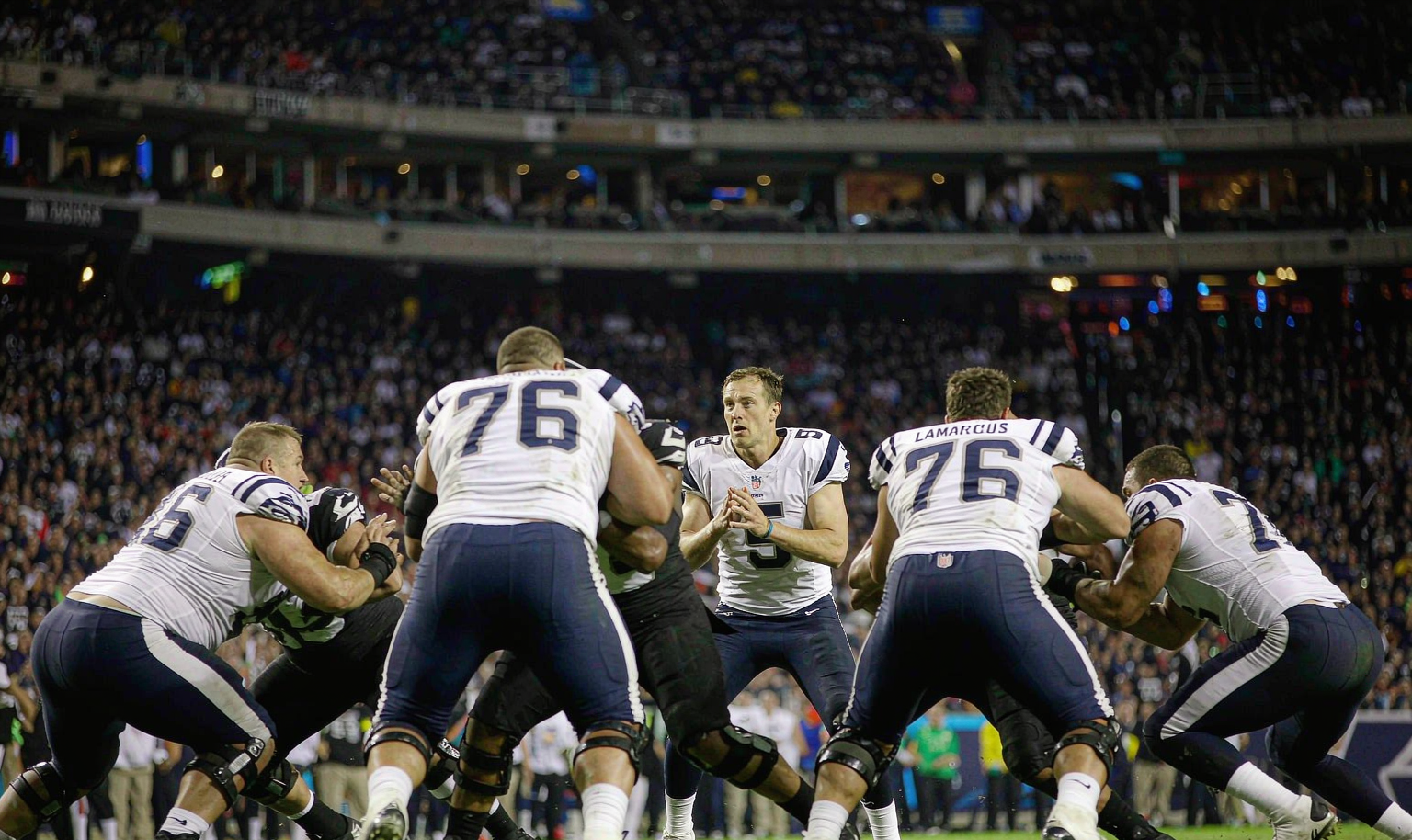 NFL quarterback scanning the field behind his line in a night game