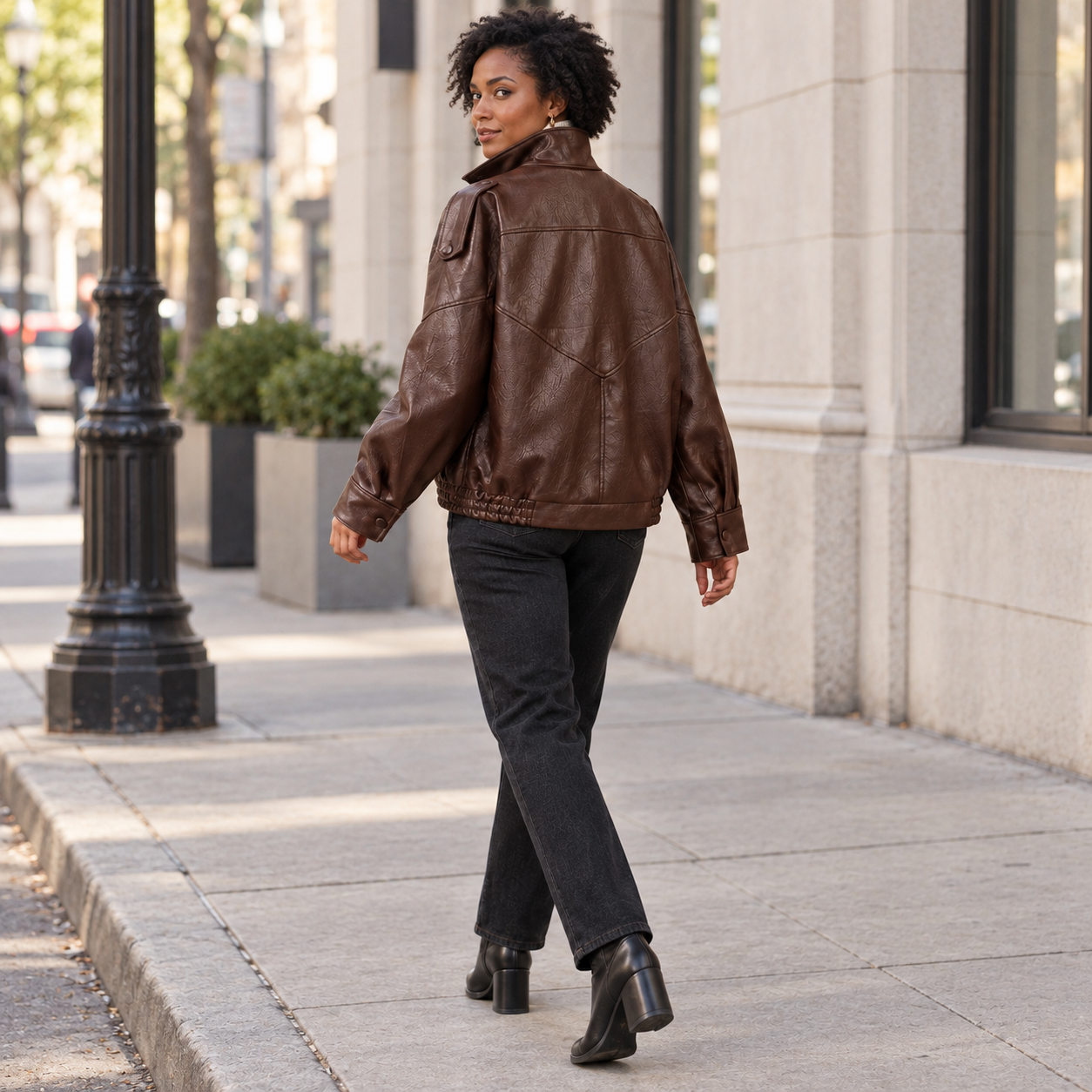 Woman wearing the Dark Brown faux-leather jacket in a natural city street back view