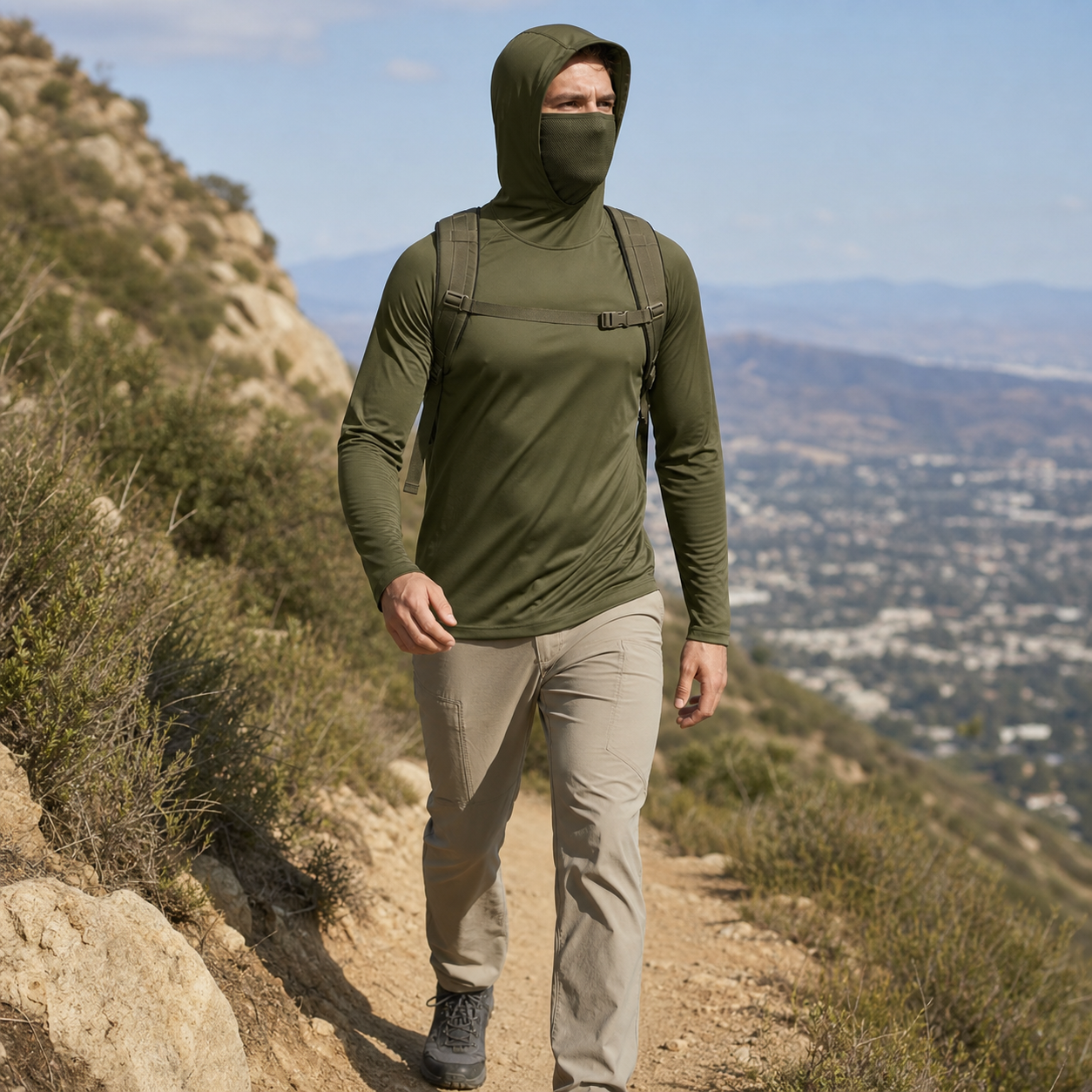 Man wearing an olive hooded performance sun hoodie while walking on a sunny trail