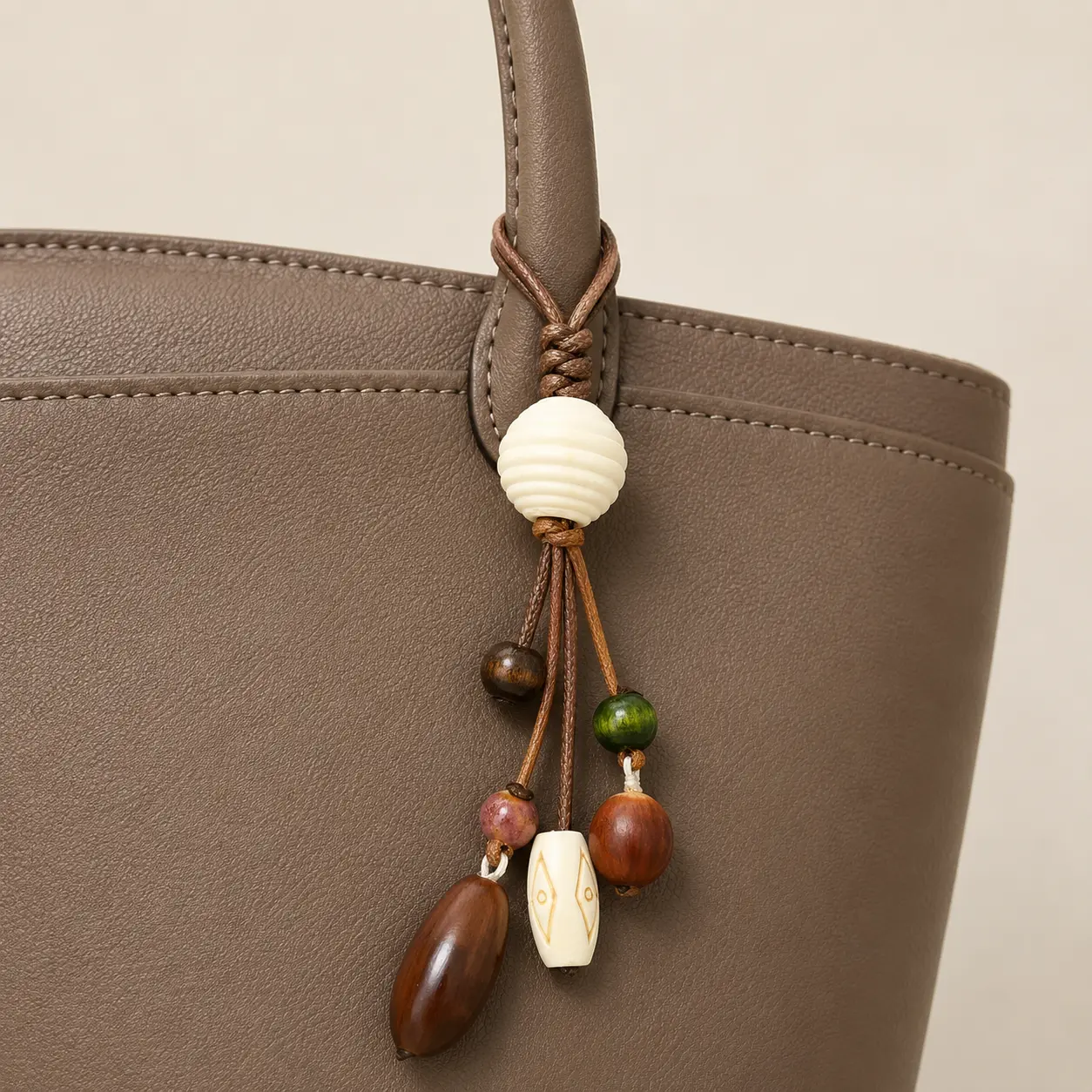 Brown loop beaded charm securely attached around a taupe handbag handle