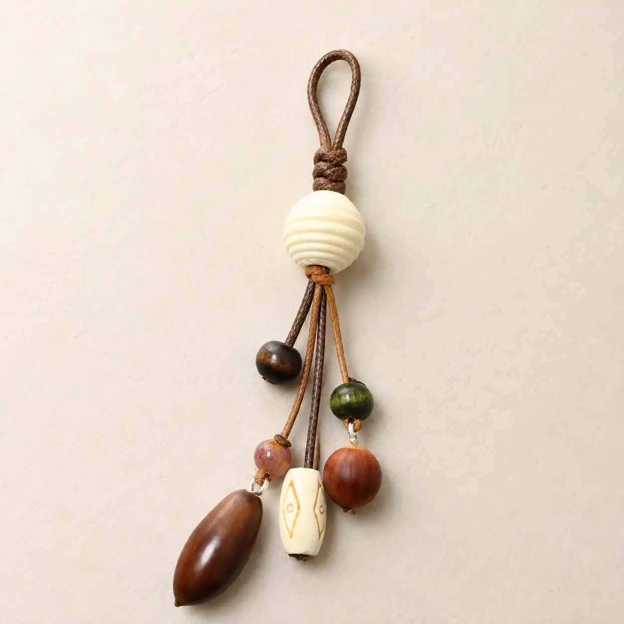 Natural-tone beaded bag charmwith brown loop, carved ivory beadand warm wood-look details