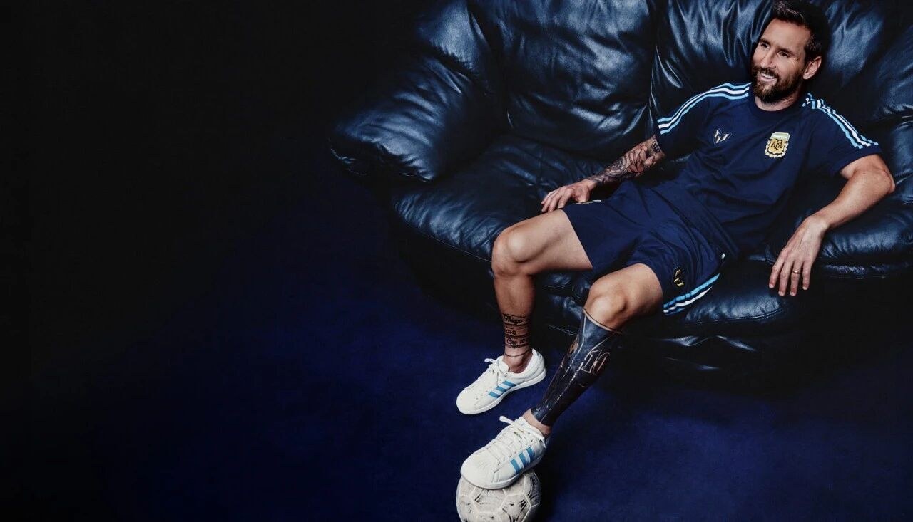 Lionel Messi sitting on a sofa in black Argentina training wear