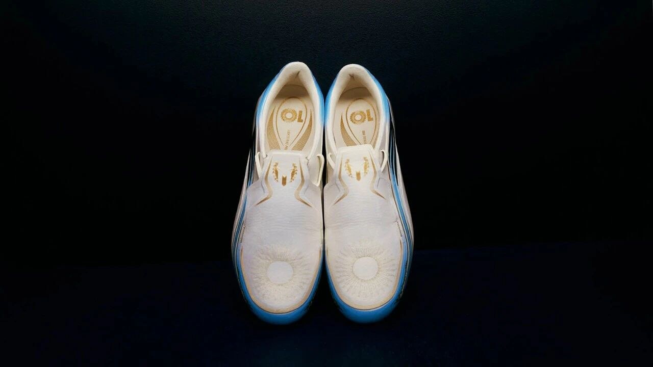 A white, mint and pink firm-ground football boot seen from above