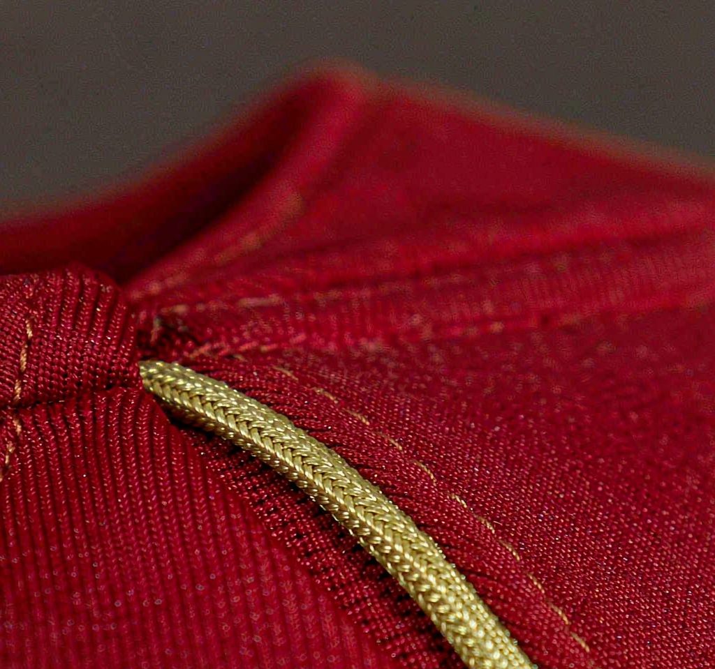 Macro close-up of crimson red football jersey fabric with warm gold trim, weave and stitching visible