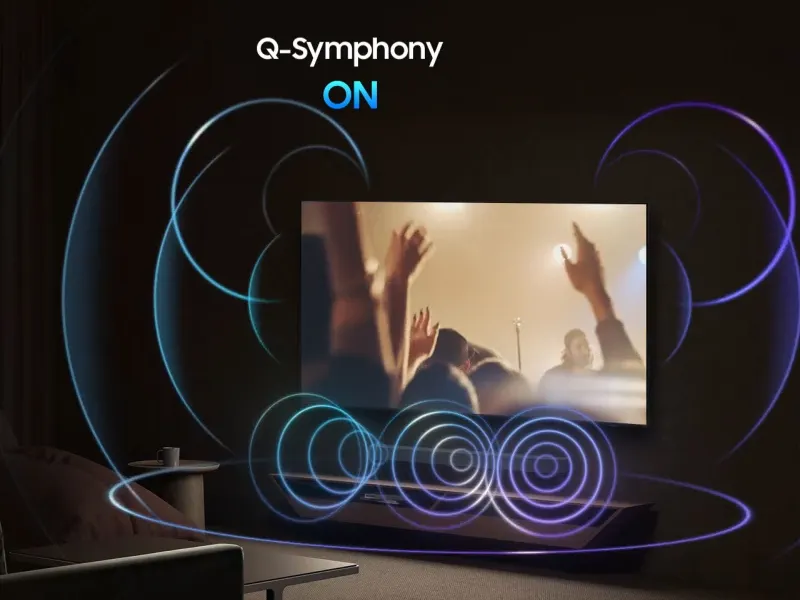 Le texte indique « Q-Symphony ON ». Appareil audio sans fil avec haut-parleurs circulaires concentriques bleus brillants et écran affichant une image aux tons chauds. Fond sombre avec visualisation sonore éclairée.