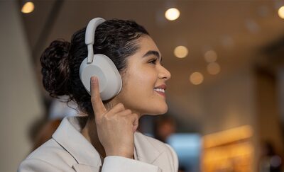 Femme utilisant un casque WH-1000XM5 dans la rue, avec la main sur l'&eacute;couteur pour activer les r&eacute;glages de commande tactile