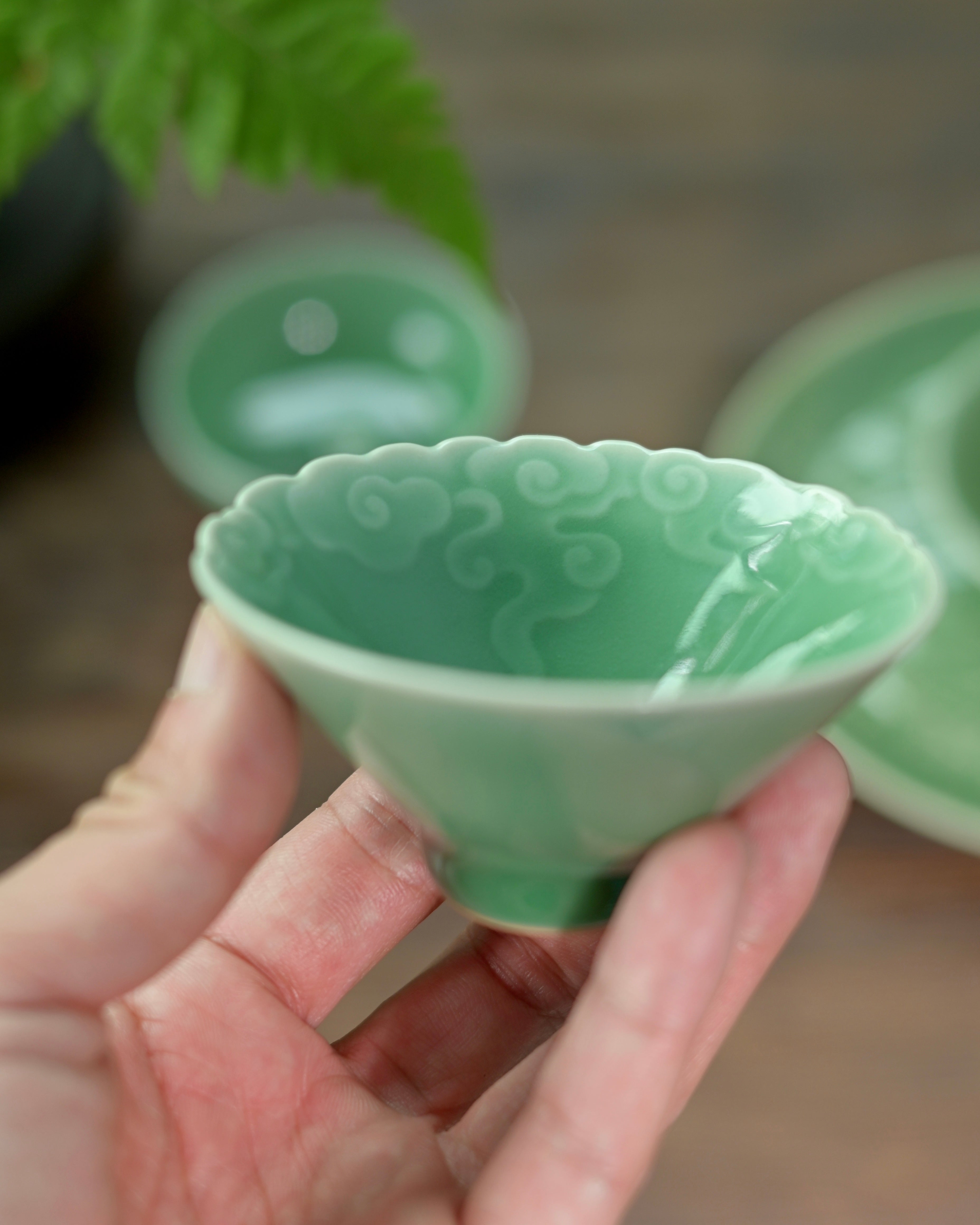 Celadon cloud teacup with intricate carving details, featuring the distinctive plum green color of Longquan porcelain by