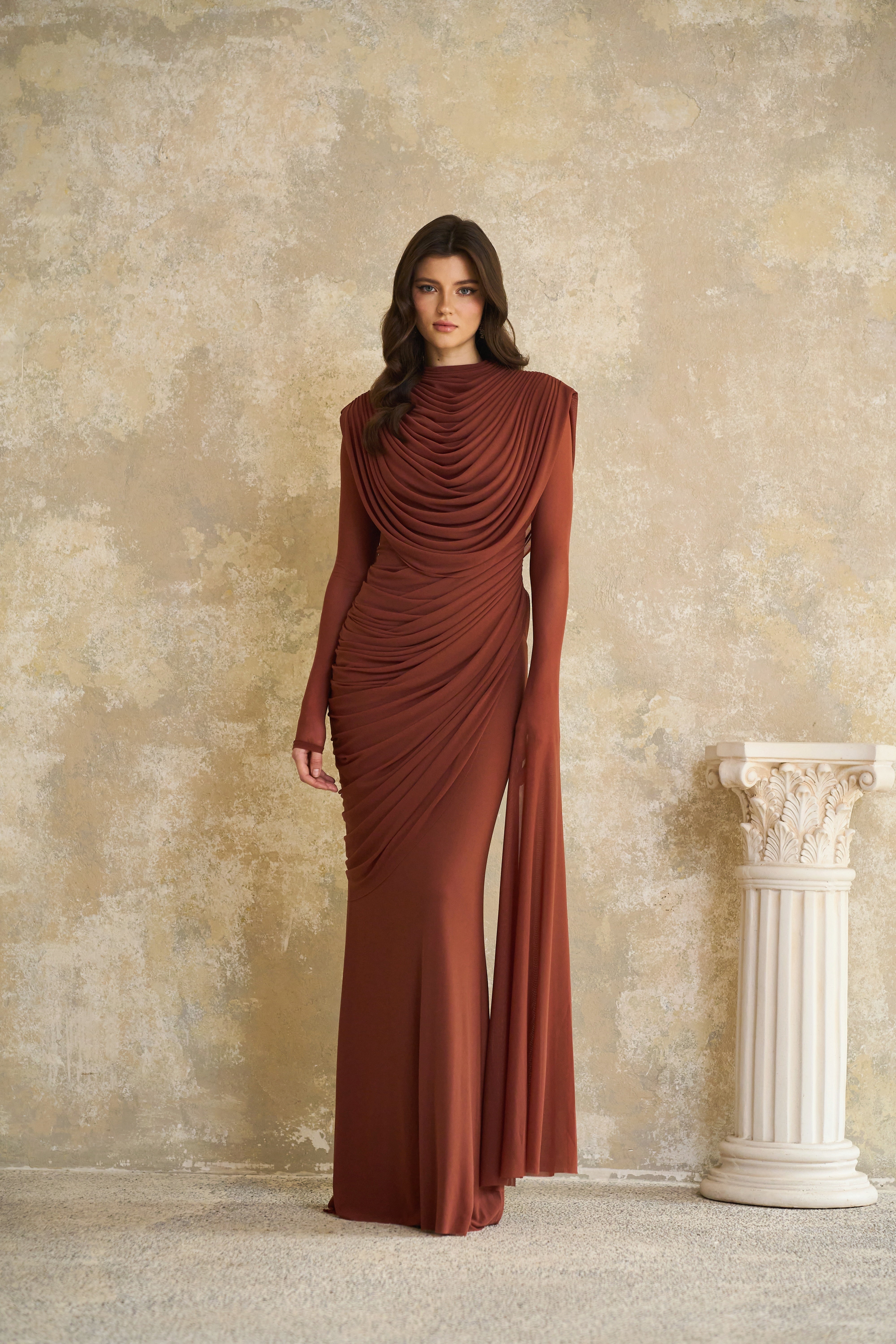 Rust-colored long-sleeve maxi dress with a draped cowl neckline and pleated bodice