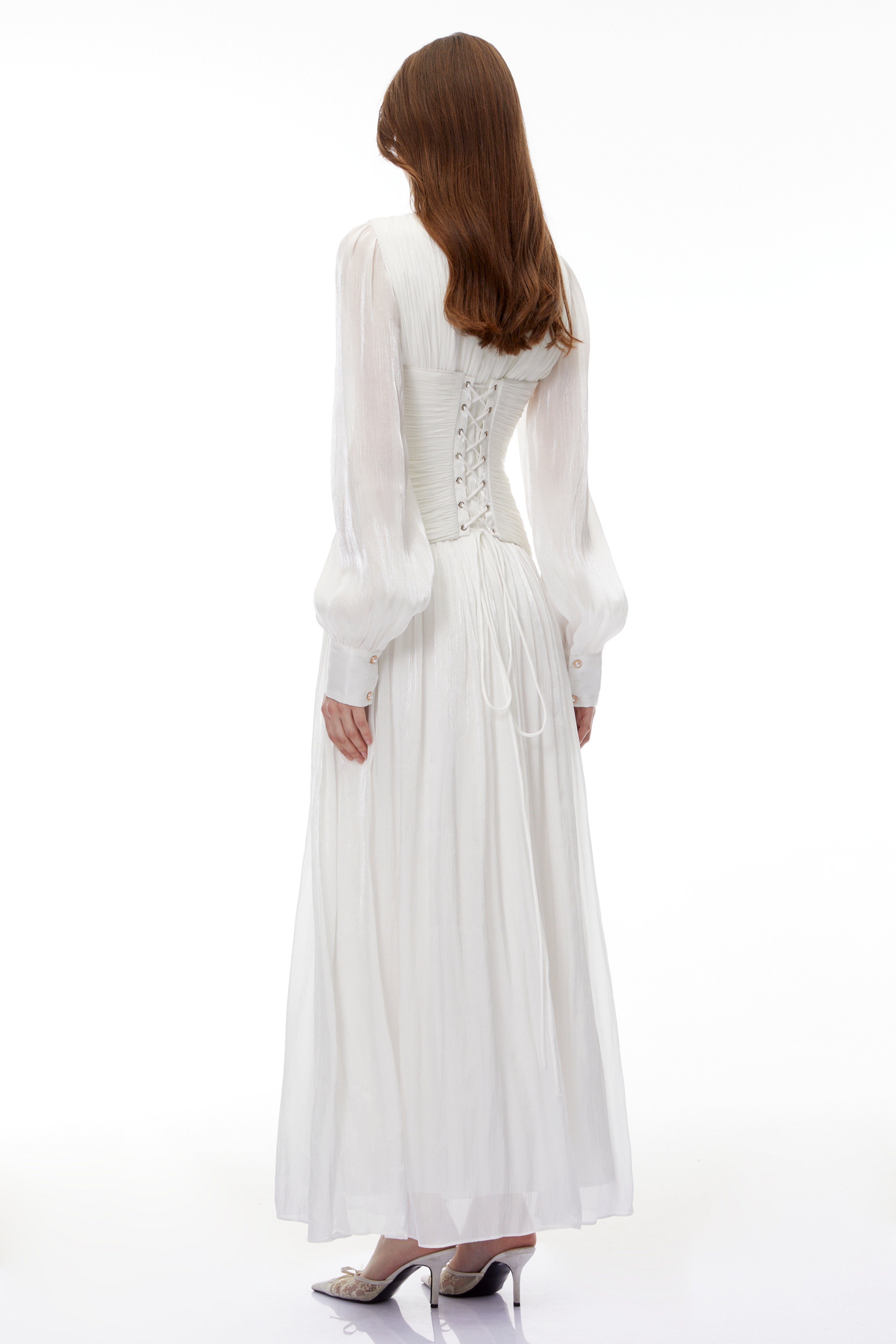 White maxi dress with a ruched bodice, round neckline, and long sheer sleeves