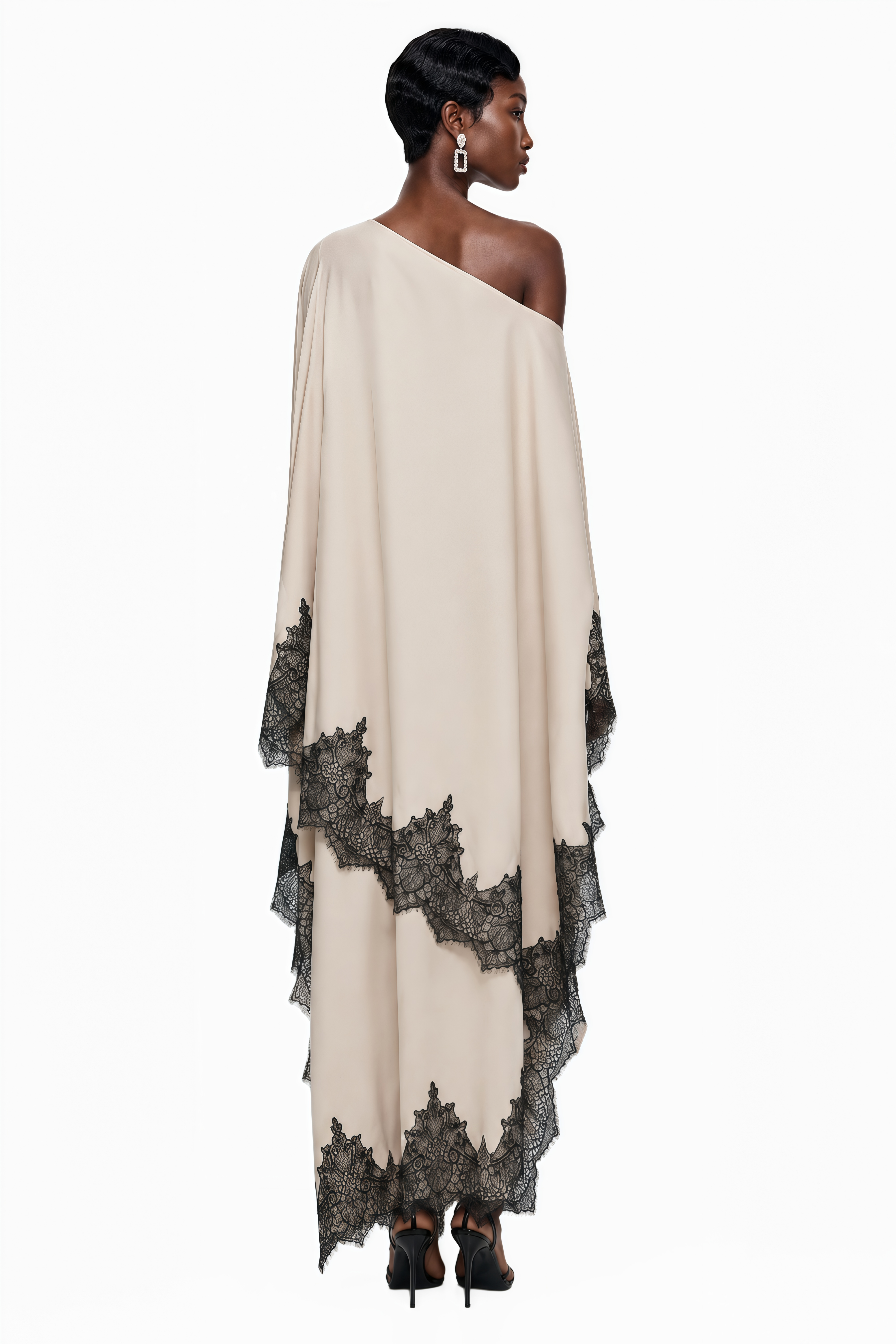 Cream one-shoulder maxi dress with an asymmetric black lace-trimmed cape and black lace-trimmed hem