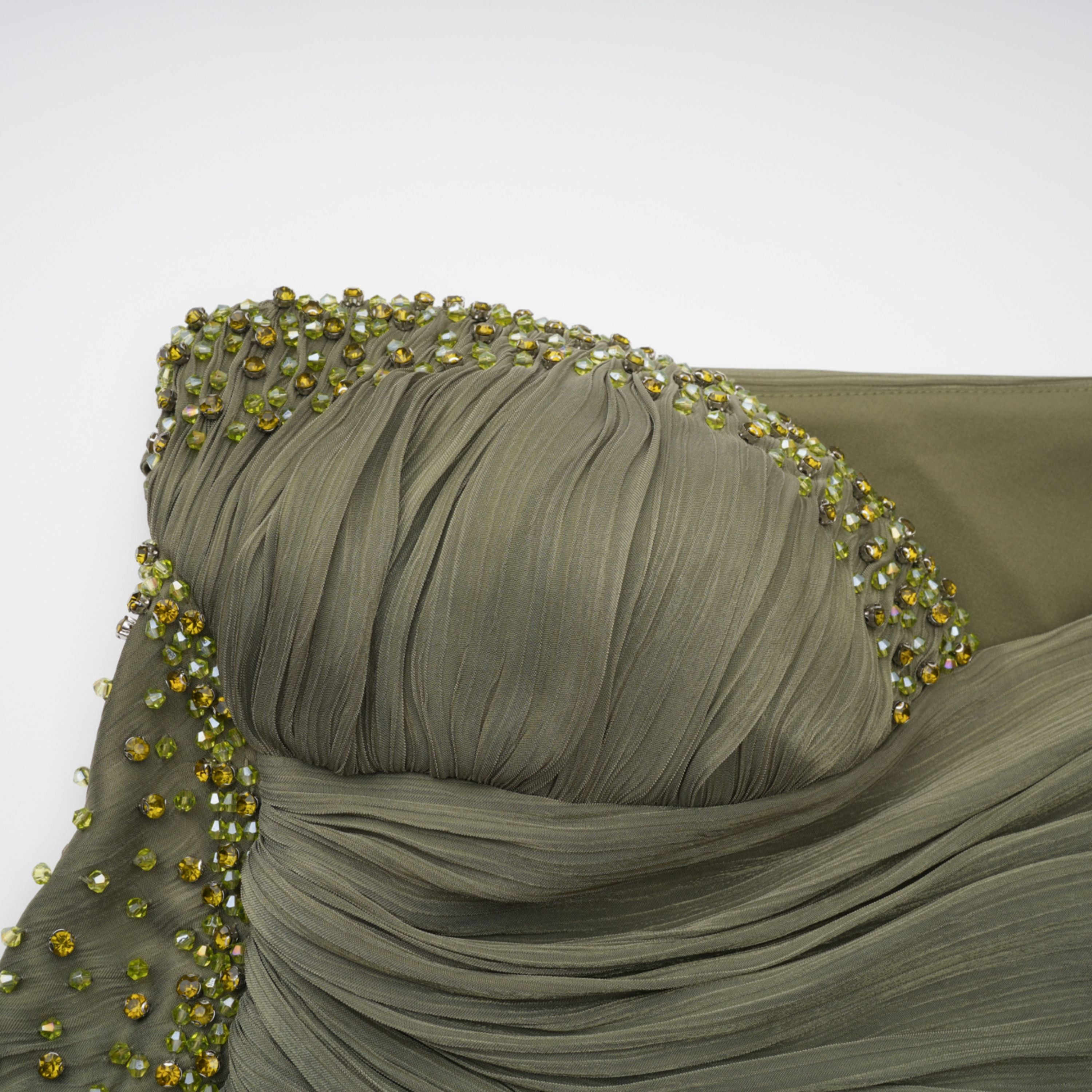 Olive green pleated one-shoulder gown with beaded embellishments and a long draped shoulder cape