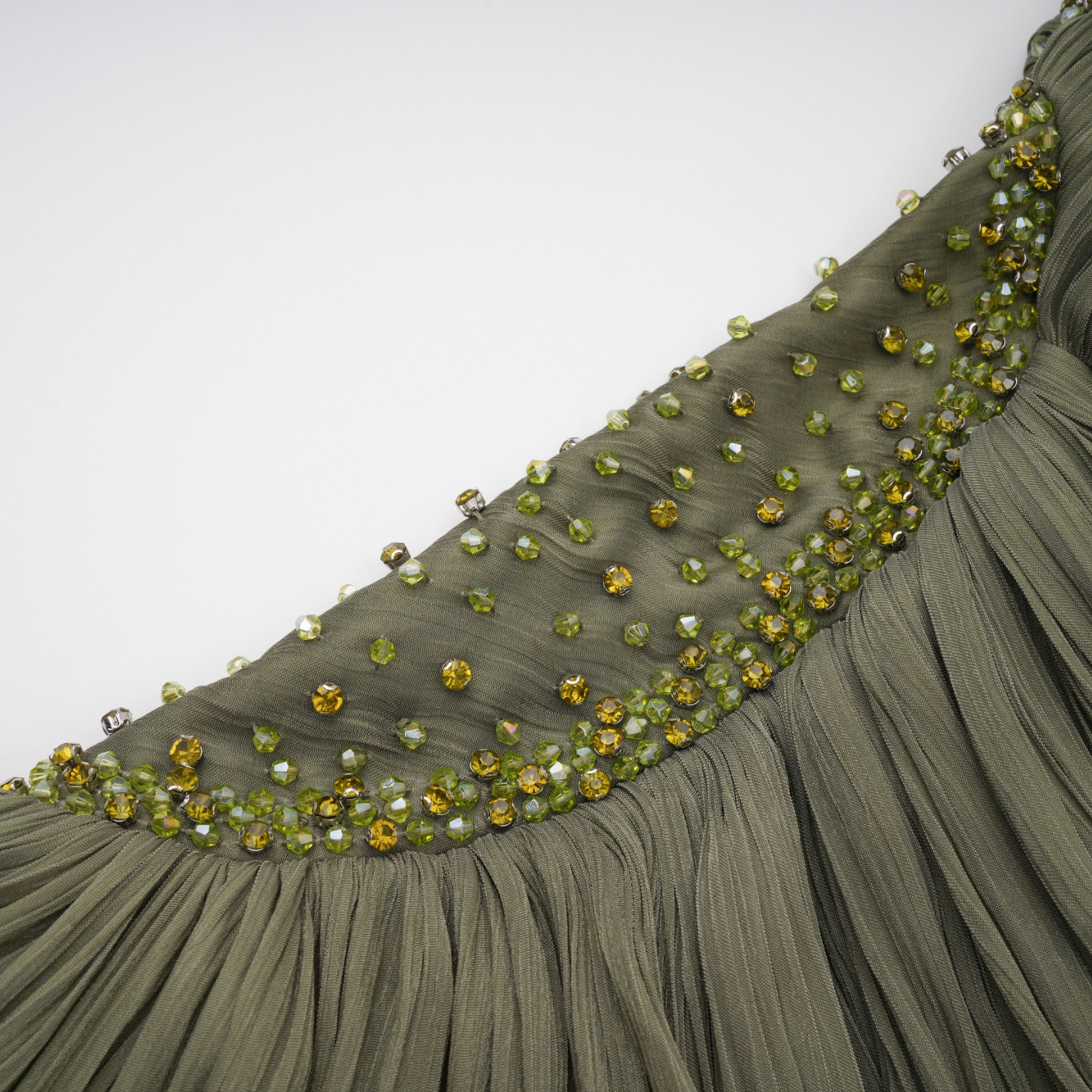 Olive green pleated one-shoulder gown with beaded embellishments and a long draped shoulder cape