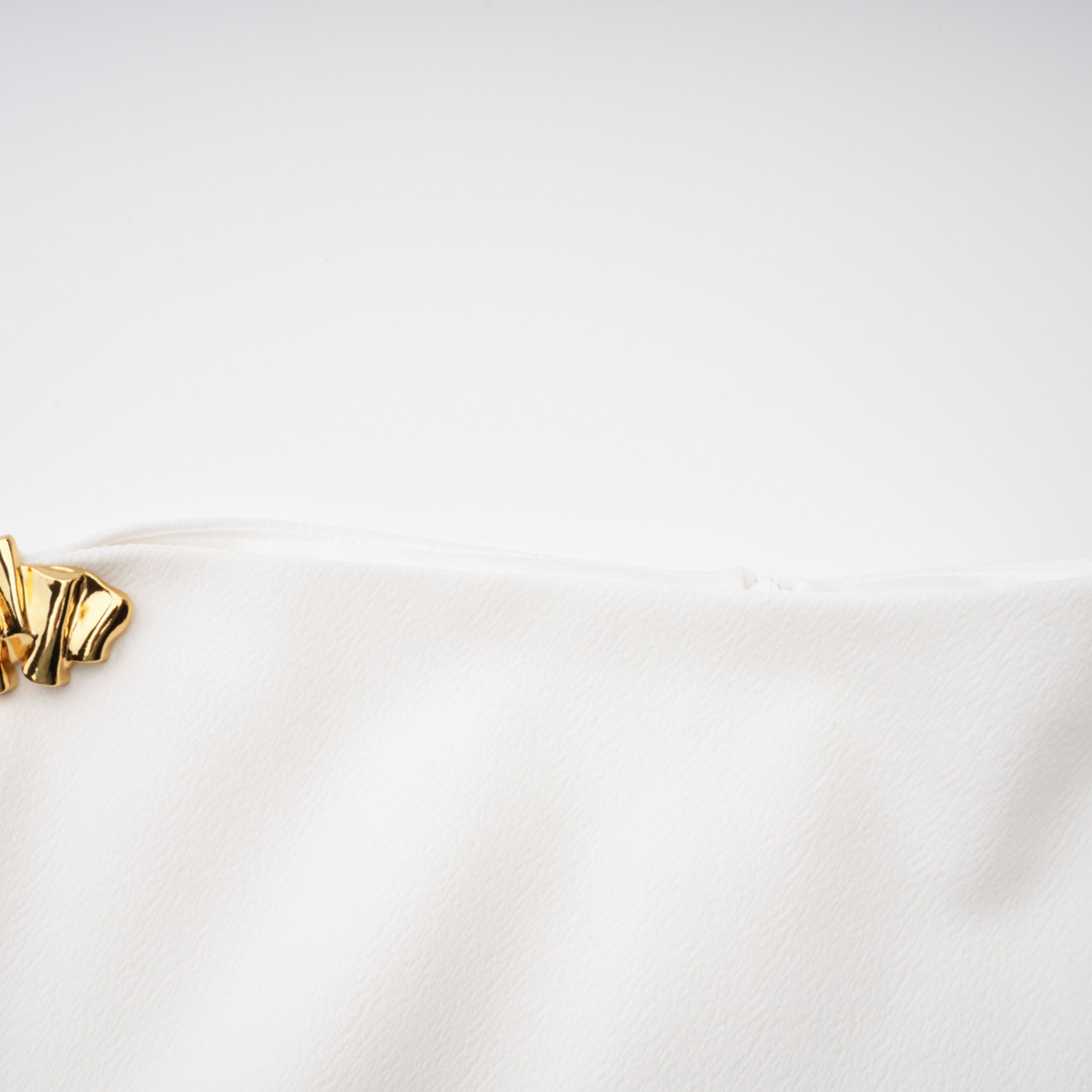 White sleeveless midi dress featuring a high drape neck with a brooch detail and a structured asymmetric handkerchief skirt