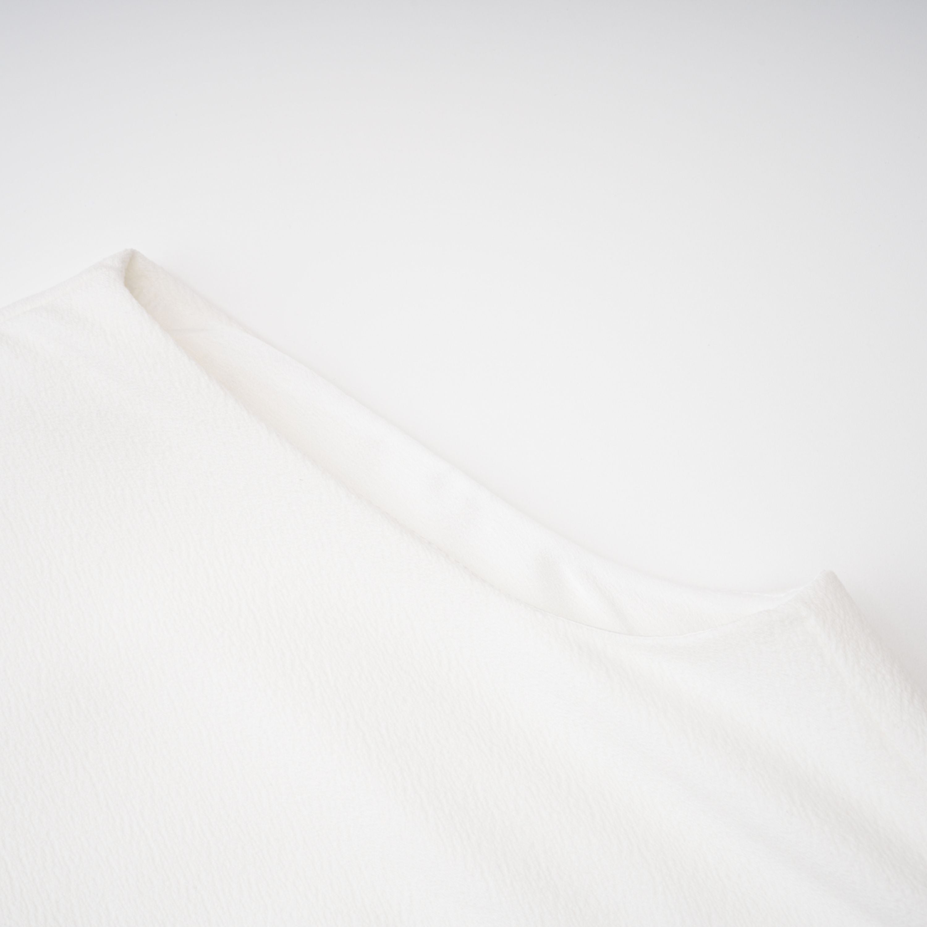 White sleeveless midi dress featuring a high drape neck with a brooch detail and a structured asymmetric handkerchief skirt