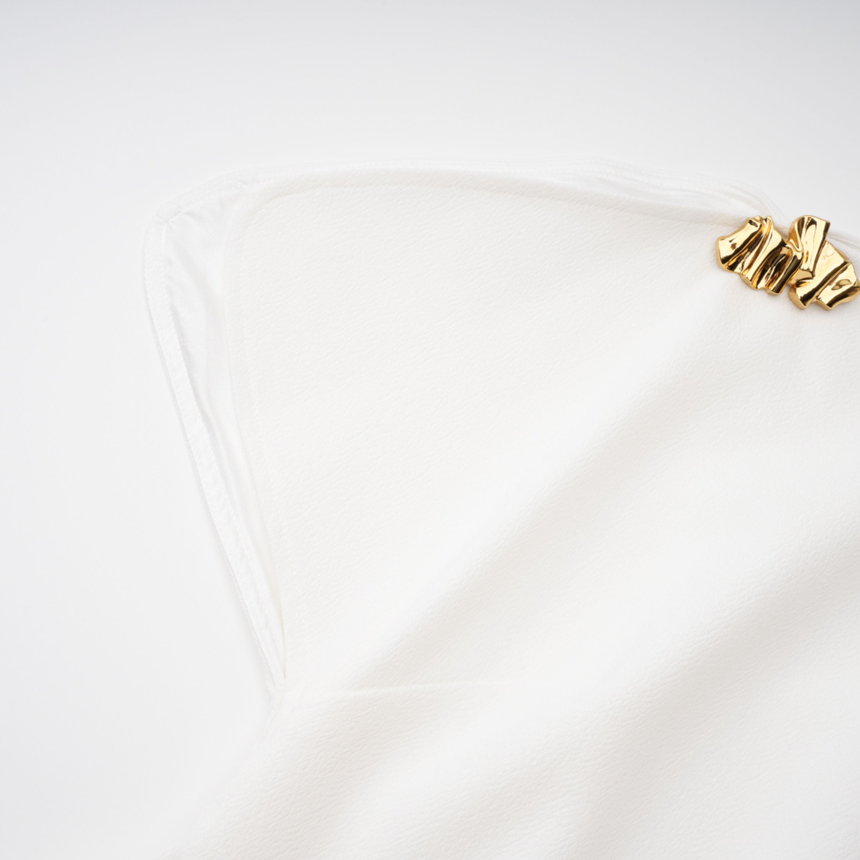 White sleeveless midi dress featuring a high drape neck with a brooch detail and a structured asymmetric handkerchief skirt