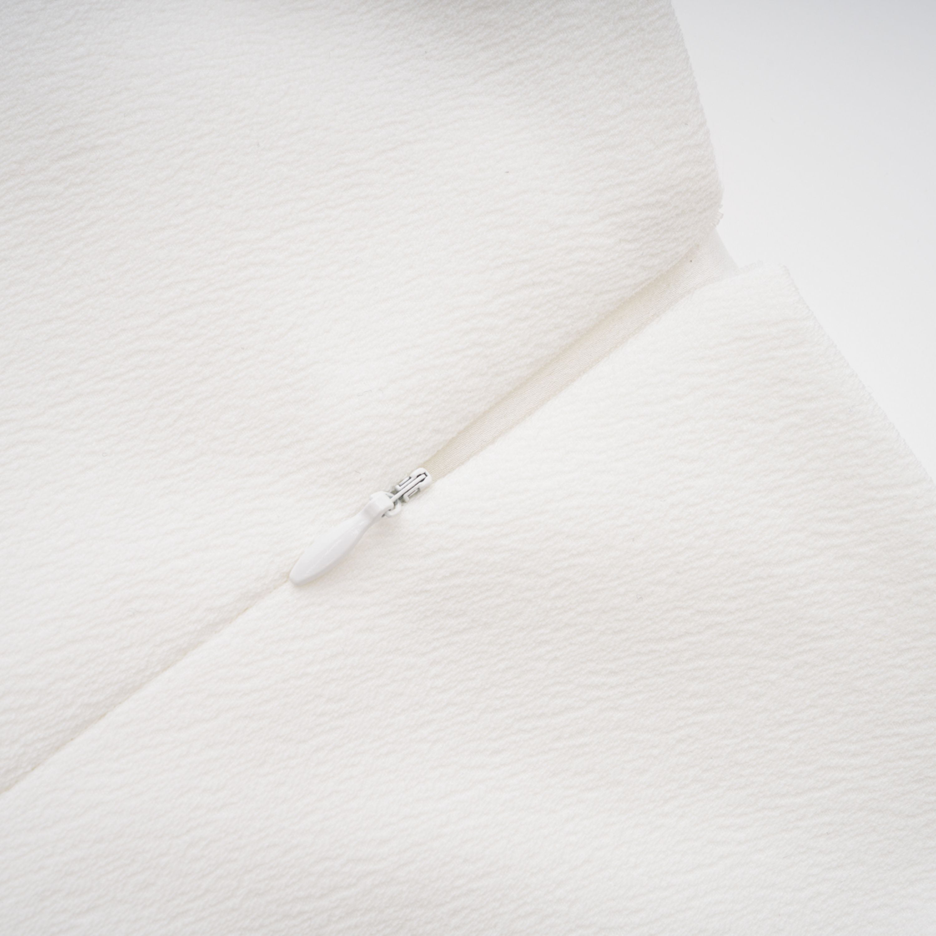 White sleeveless midi dress featuring a high drape neck with a brooch detail and a structured asymmetric handkerchief skirt
