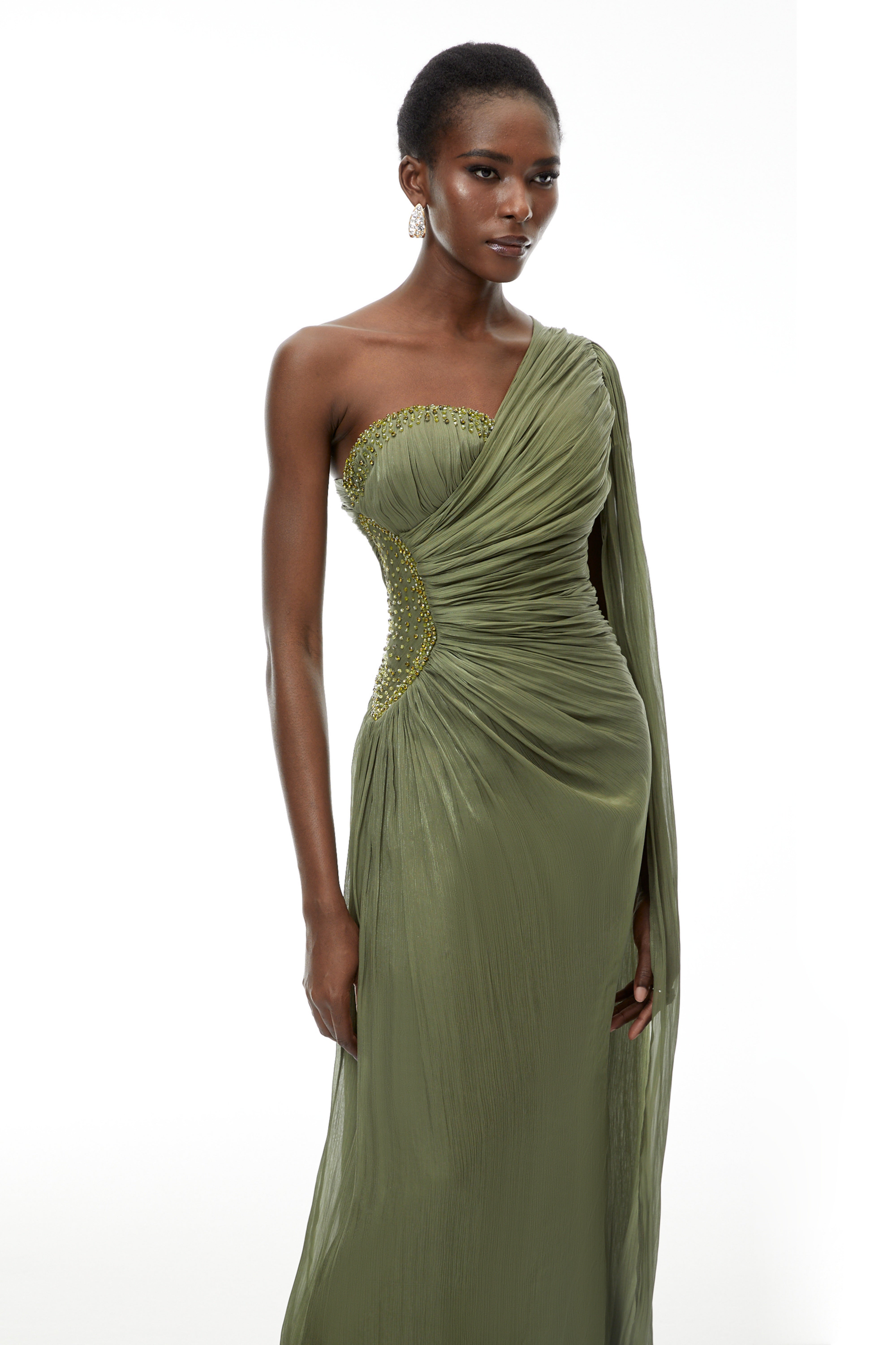 Olive green pleated one-shoulder gown with beaded embellishments and a long draped shoulder cape