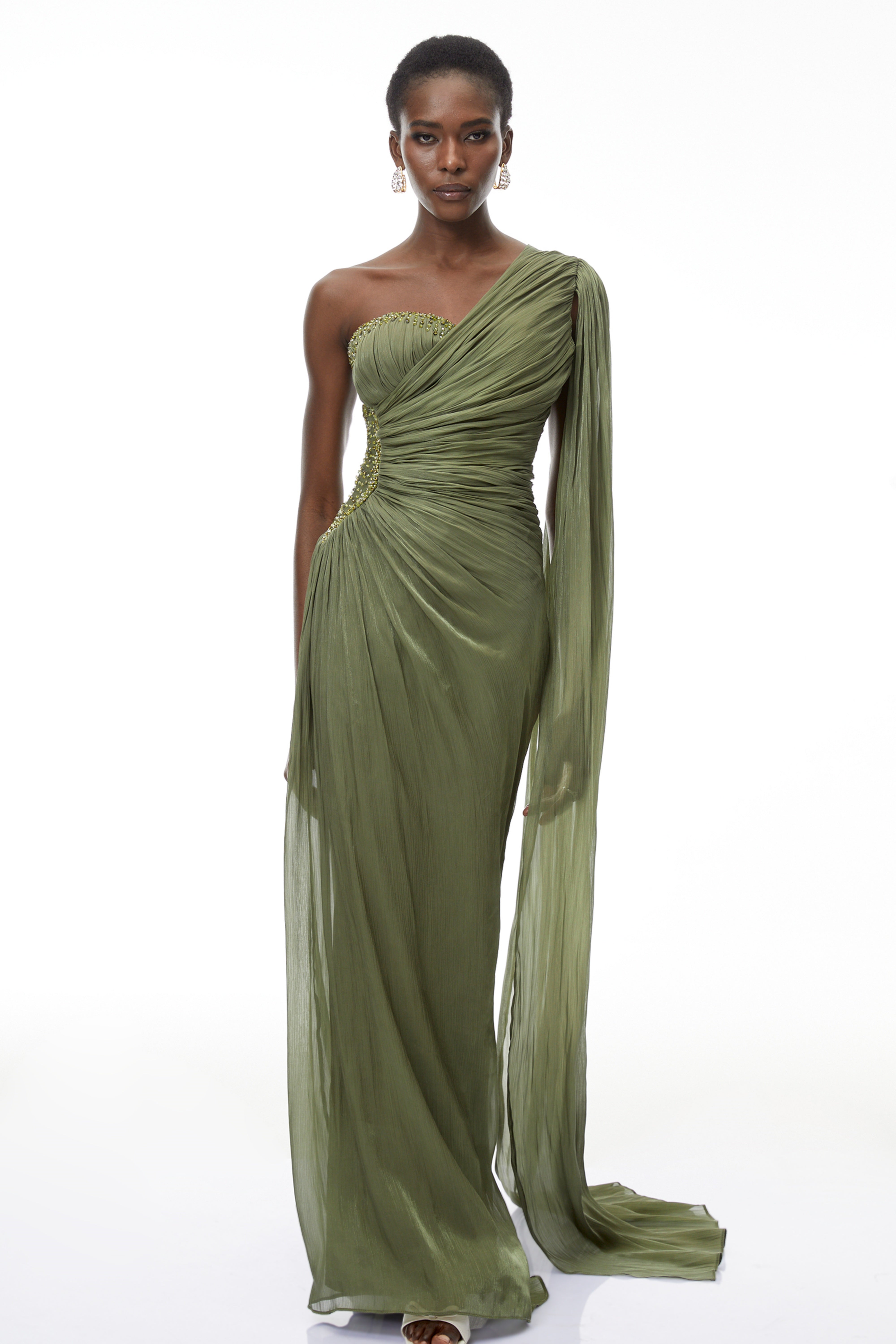 Olive green pleated one-shoulder gown with beaded embellishments and a long draped shoulder cape