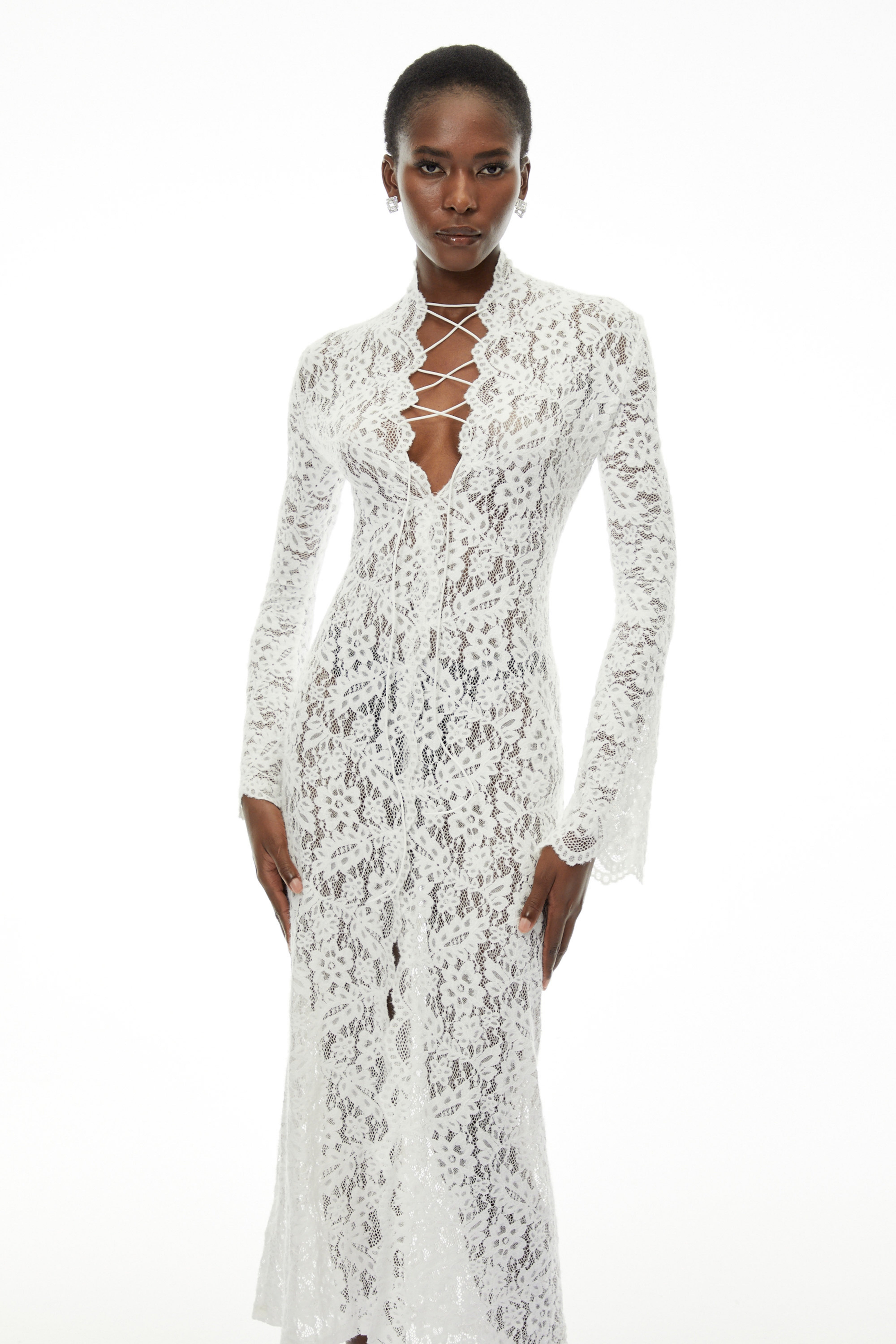 White lace maxi dress with a lace-up plunging neckline, long flared sleeves, and a high front slit
