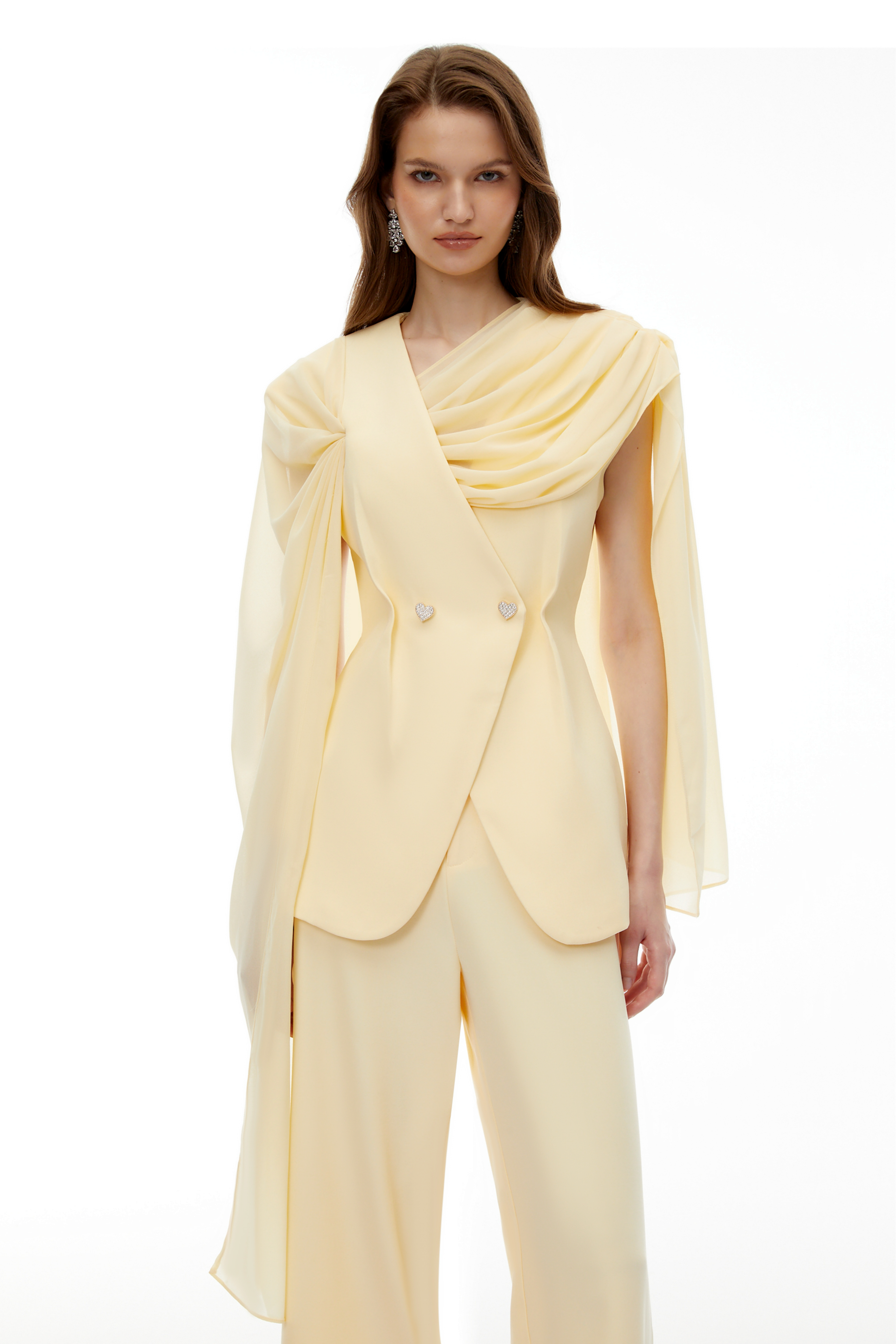 Pale yellow top and trousers set with an asymmetric blazer bodice, draped sheer neckline, and cape panels