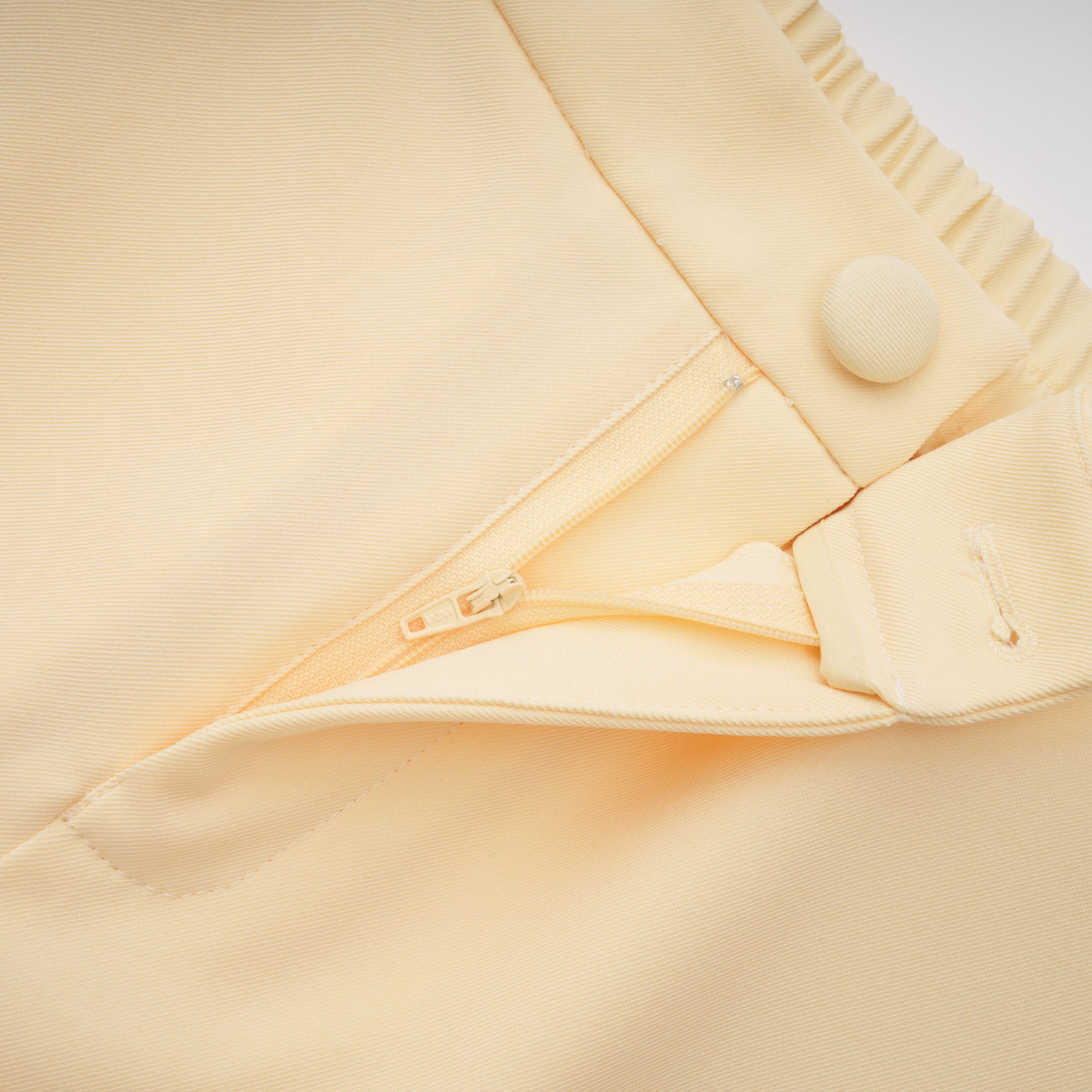 Pale yellow top and trousers set with an asymmetric blazer bodice, draped sheer neckline, and cape panels