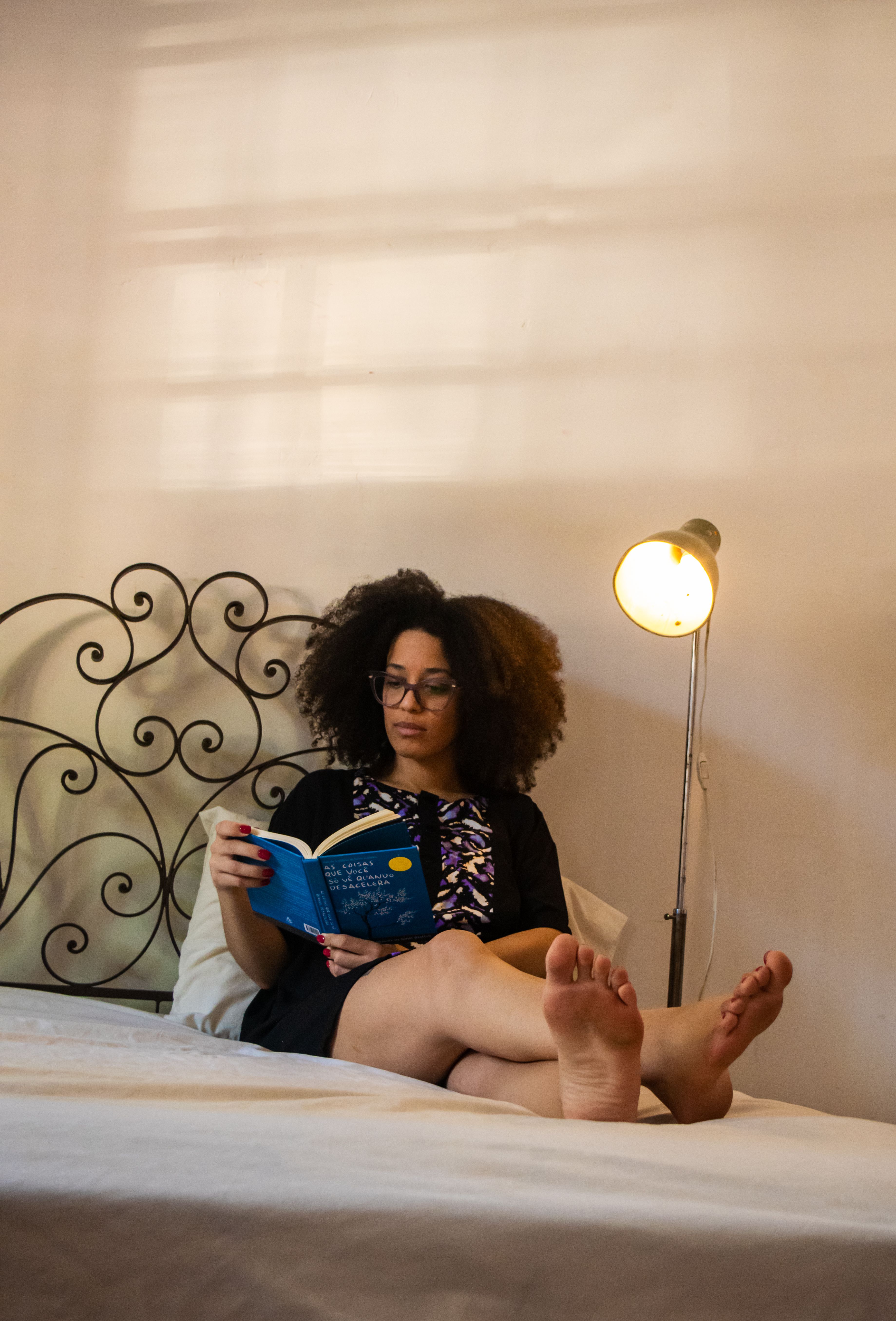 Mulher adulta l&ecirc; em um quarto iluminado por uma lumin&aacute;ria, em um momento de descanso e autocuidado.