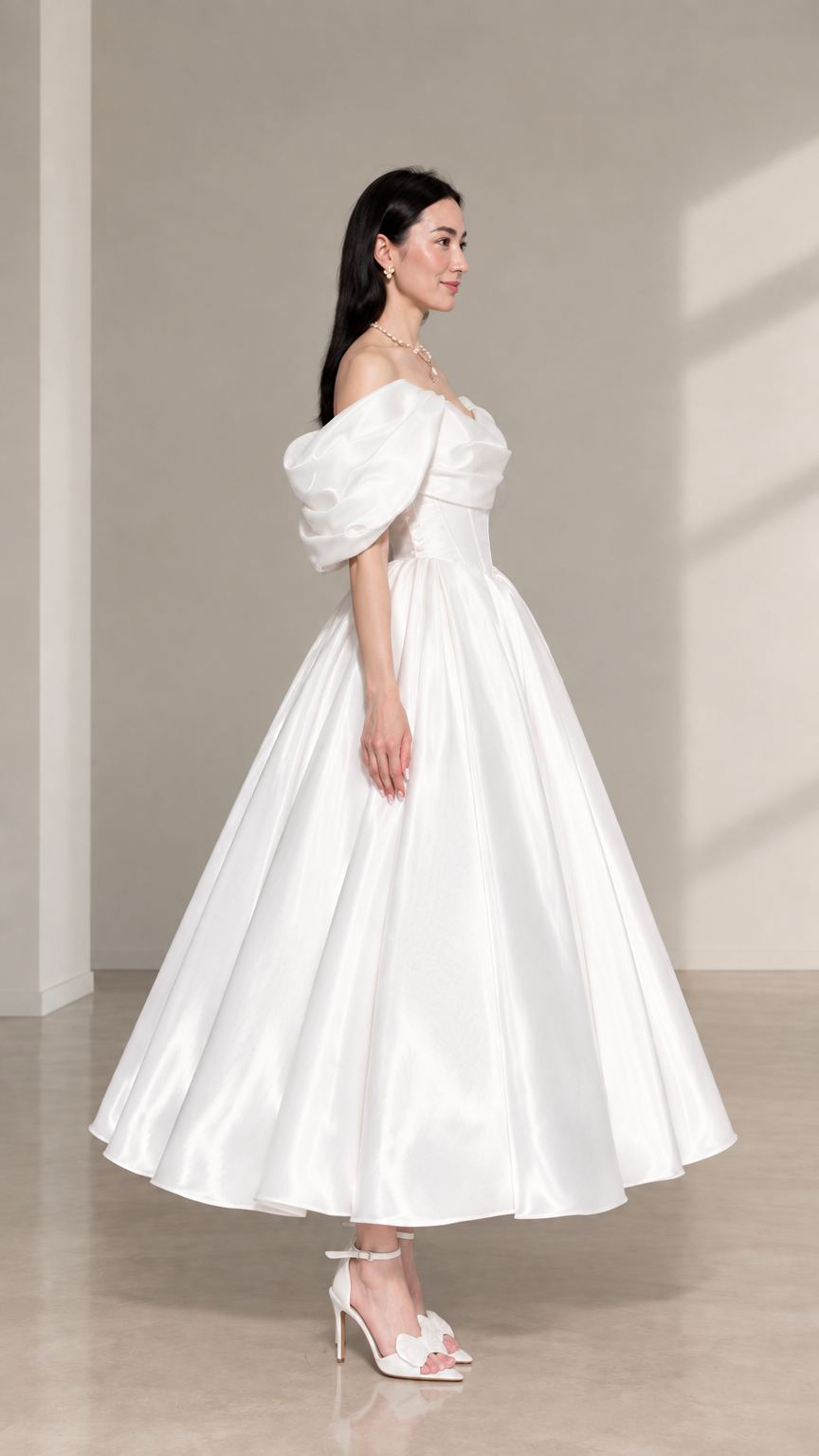 Side-angle view of white off-the-shoulder satin midi evening dress with pleated skirt