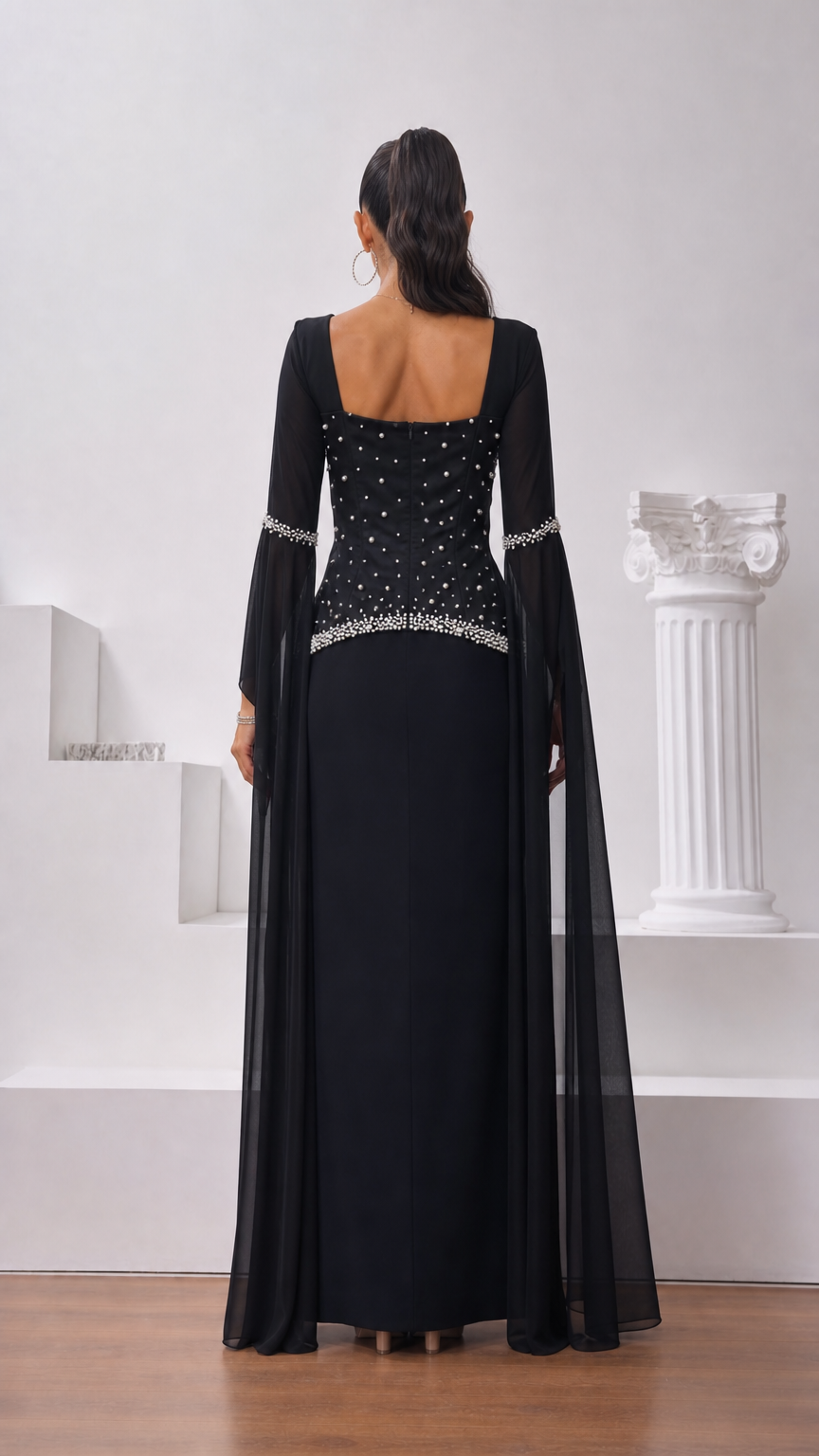 Back view of model wearing black floor-length formal gown with pearl accents and square neckline