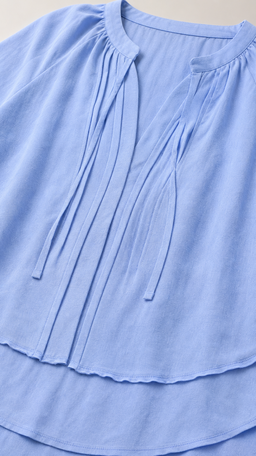 Close-up detail of pleated notch neckline and double-layered tiered hem on Light Blue blouse