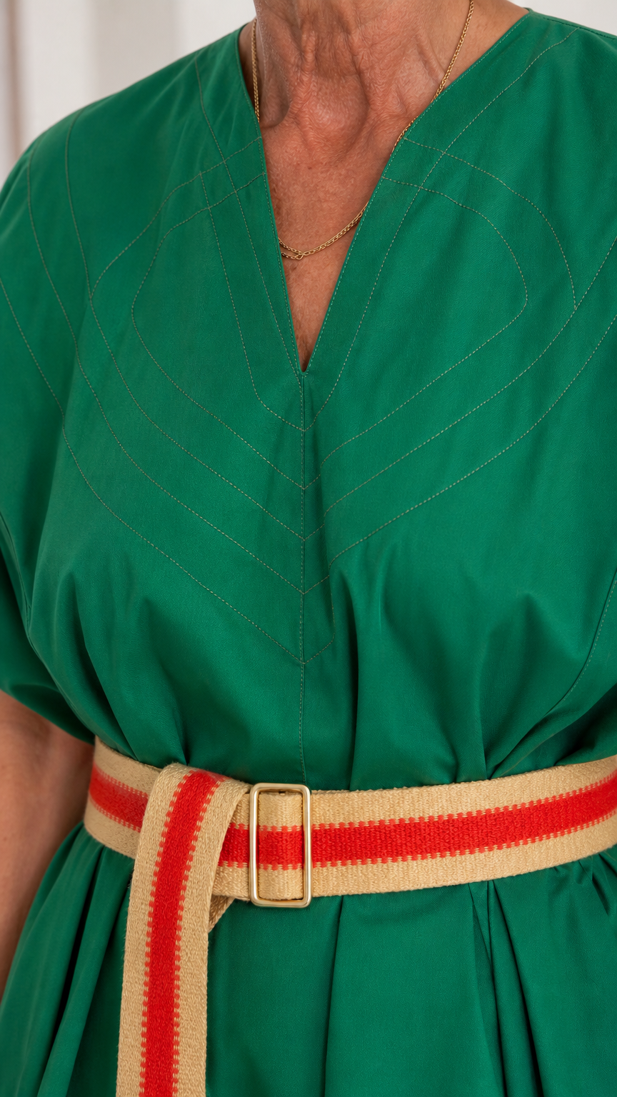 Close-up detail of V-neck topstitching and striped buckle belt on green maxi dress