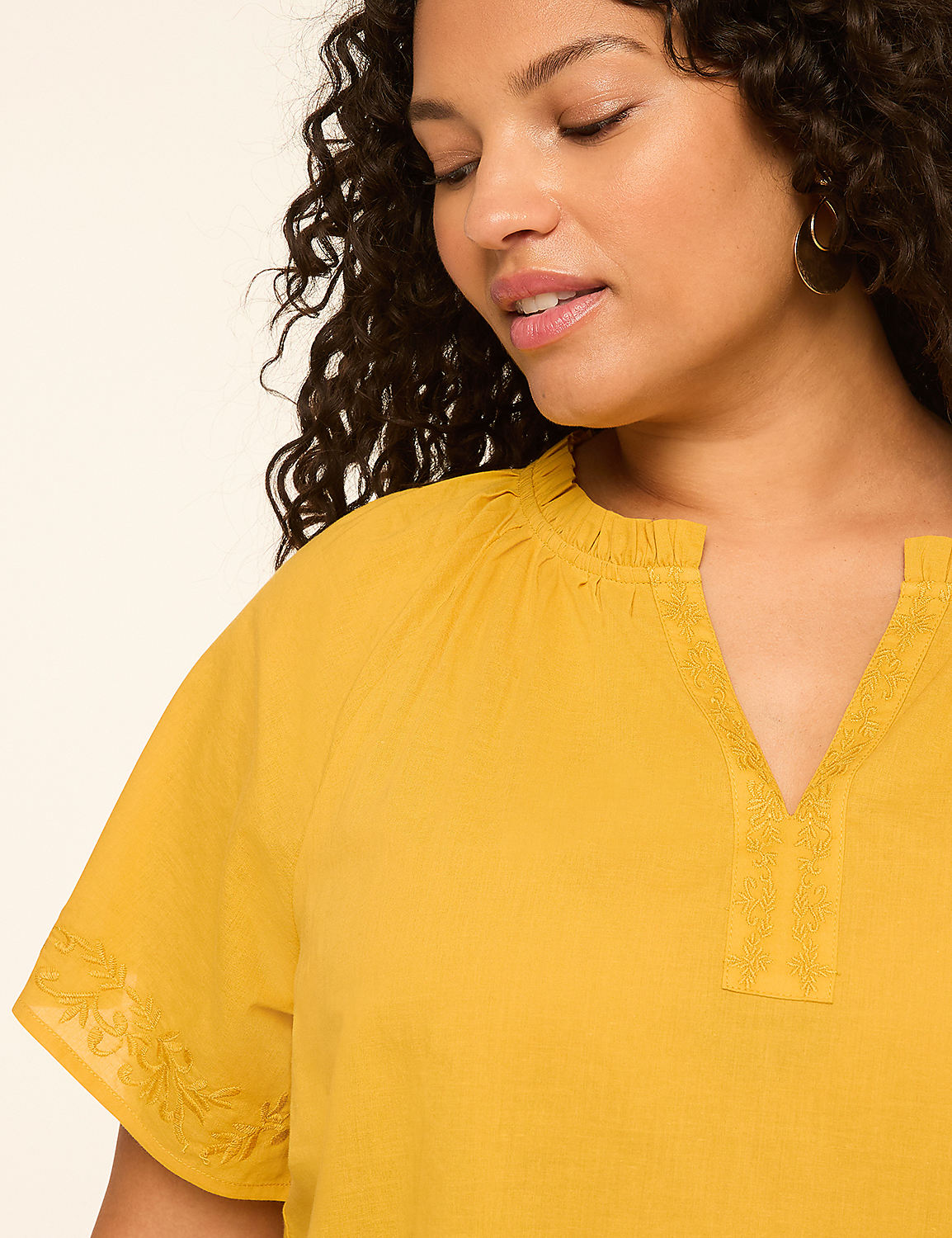 A woman with curly dark hair wears a yellow top with embroidered details, against a plain, light-colored background. Product Image 4