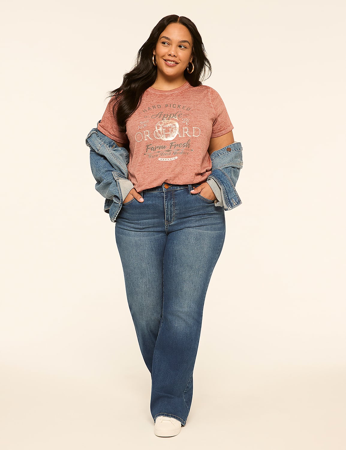 A woman in a pink graphic t-shirt, white jacket, and blue jeans stands against a plain, light-colored background. Product Image 3