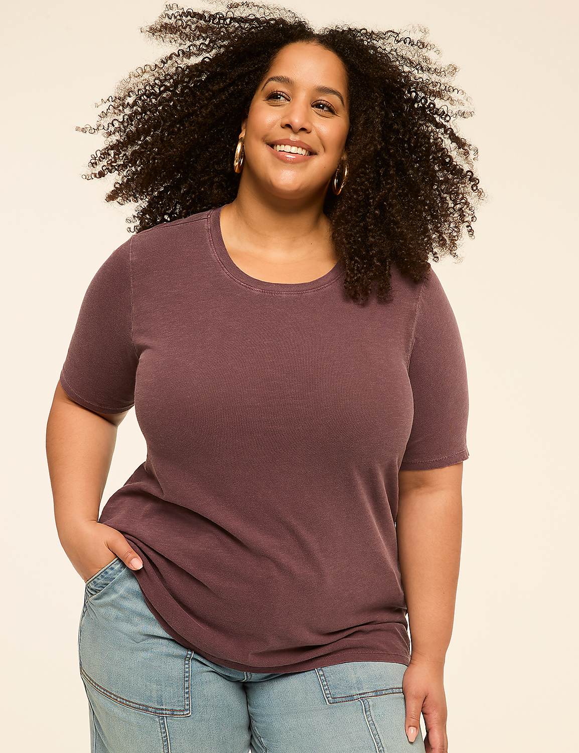 A smiling woman with curly hair in a purple t-shirt and jeans stands against a plain, light-colored background. Product Image 1