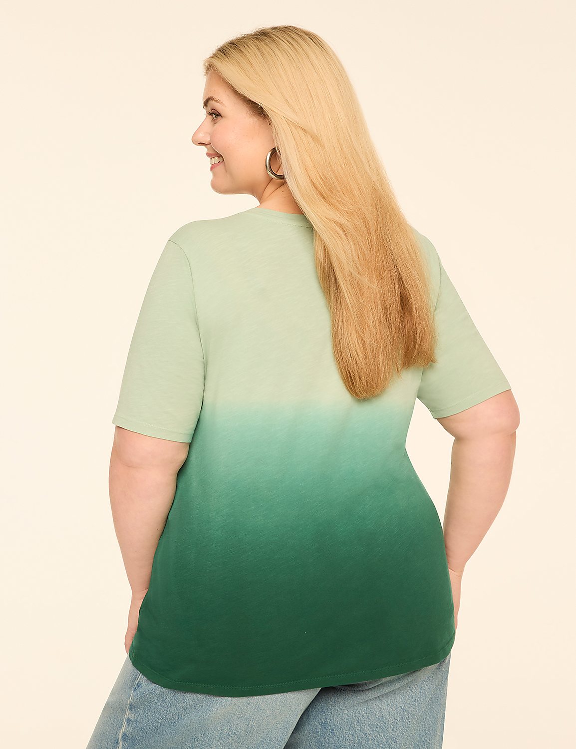 A woman with blonde hair, wearing a green ombre t-shirt and blue jeans, smiles as she stands against a plain, light-colored background. Product Image 2
