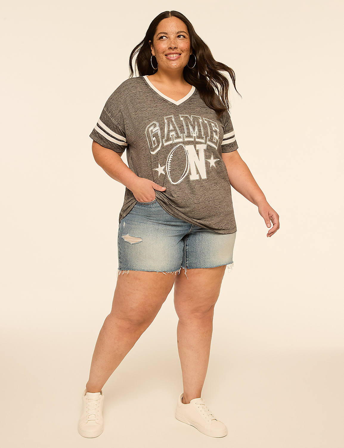 A woman in a "Game On" t-shirt and denim shorts stands against a plain, light-colored background. Product Image 3