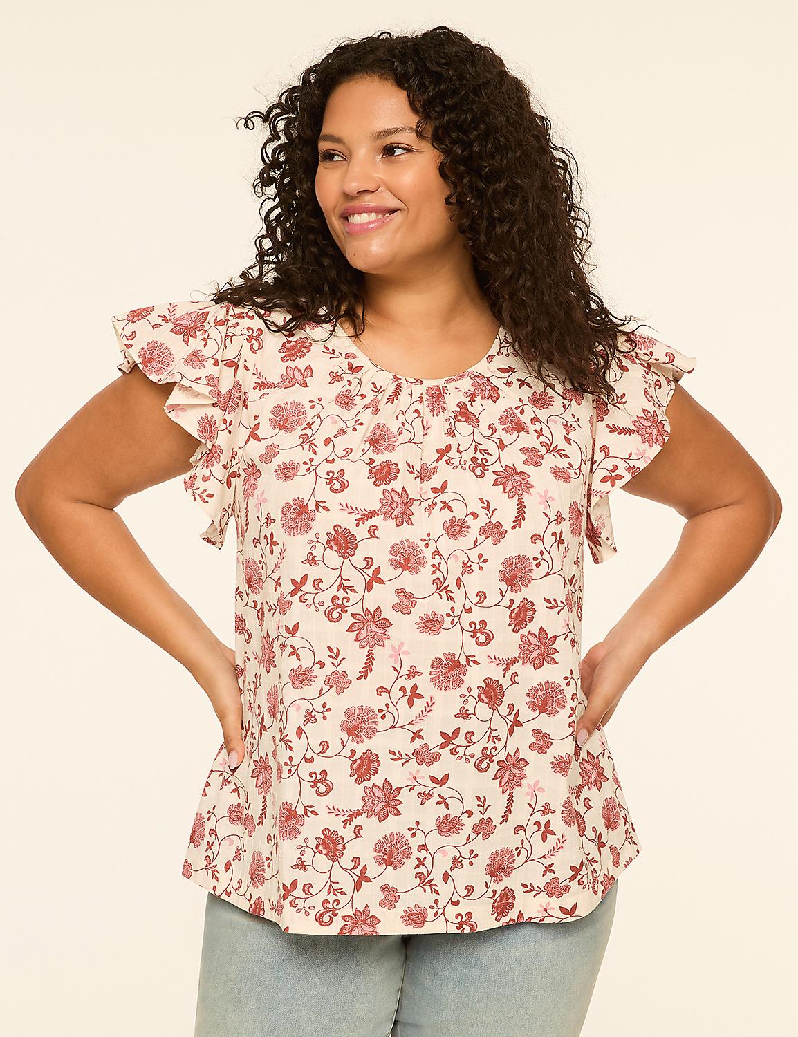 A smiling woman with curly dark hair poses with her hands on her hips, wearing a cream-colored floral print top with ruffled sleeves, against a plain cream background. Product Image 1