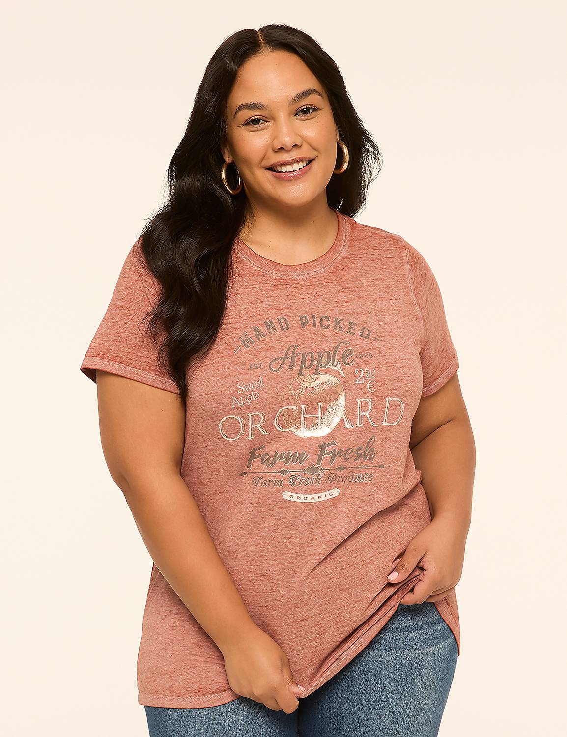 A woman in a pink t-shirt with an apple orchard graphic stands against a plain, light-colored background. Product Image 1