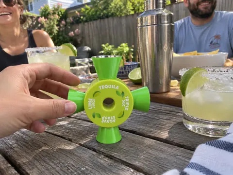 Green four-way cocktail jigger beside margaritas at a backyard gathering