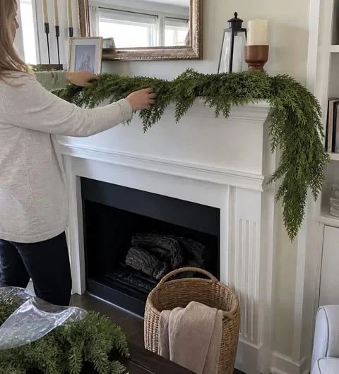 Mantel greenery being fluffed in a bright living room