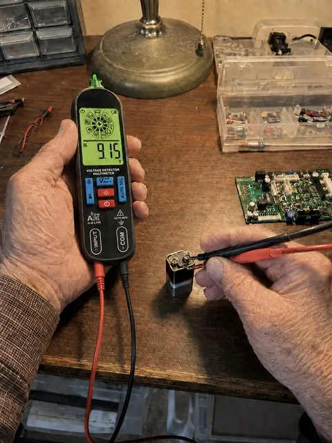 Smart pen multimeter checking a battery at a home electronics desk