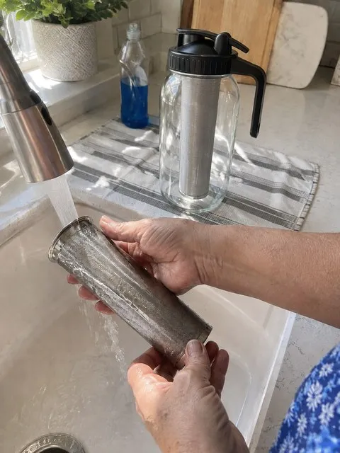 Stainless steel mesh infuser being rinsed at a kitchen sink