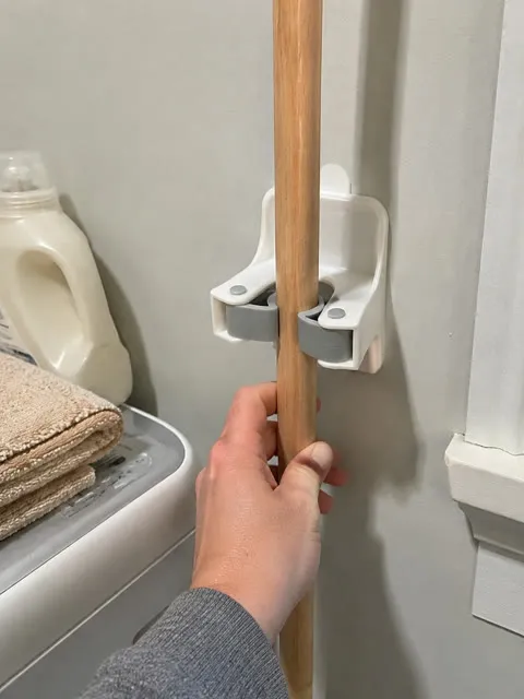 Hand placing a broom handle into a wall gripper beside a washer